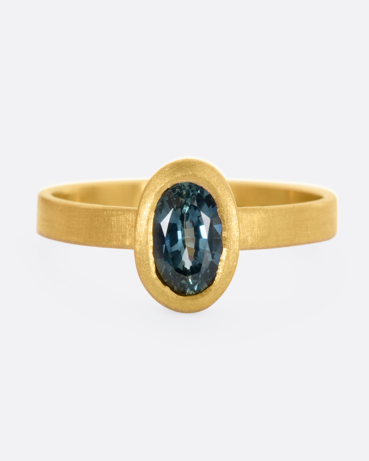 A matte yellow gold ring with an oval blue sapphire. View from the front.