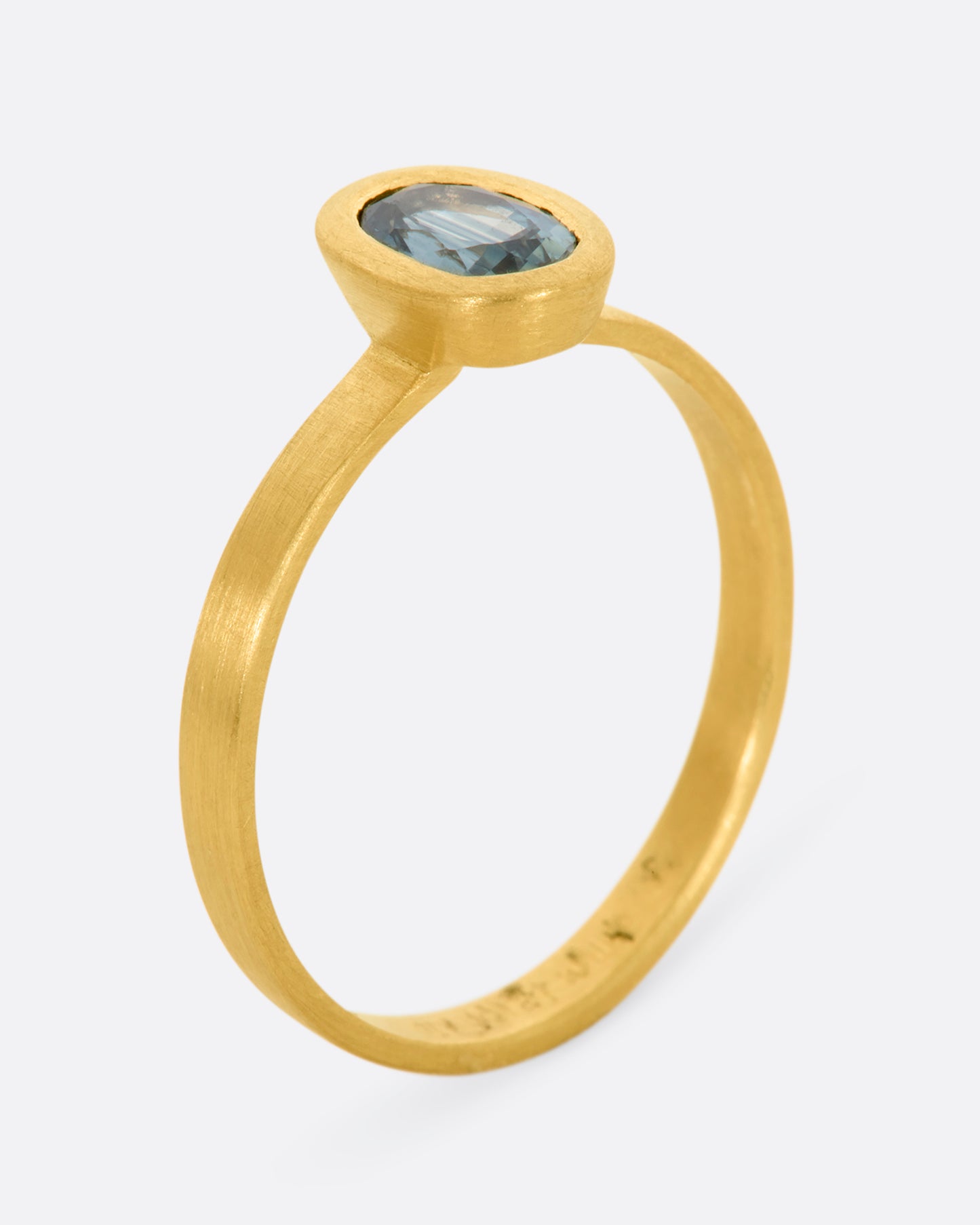 A matte yellow gold ring with an oval blue sapphire. View from the side standing.