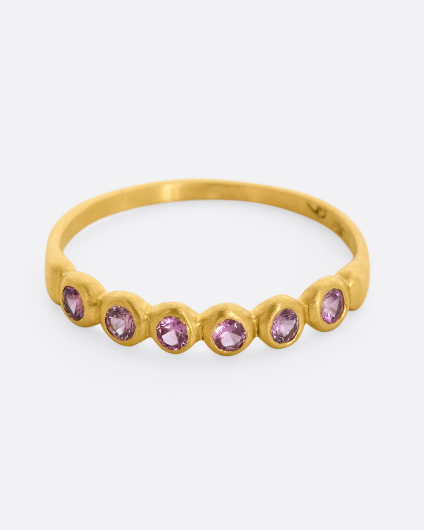 A yellow gold band with a row of pink sapphires. Shown from the front, from slightly above.