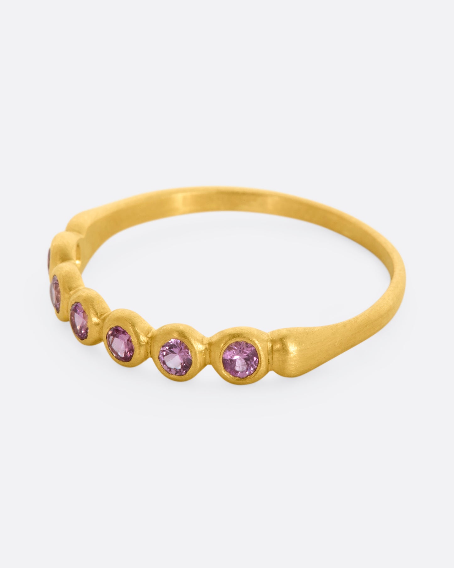 A yellow gold band with a row of pink sapphires. Shown from the side.