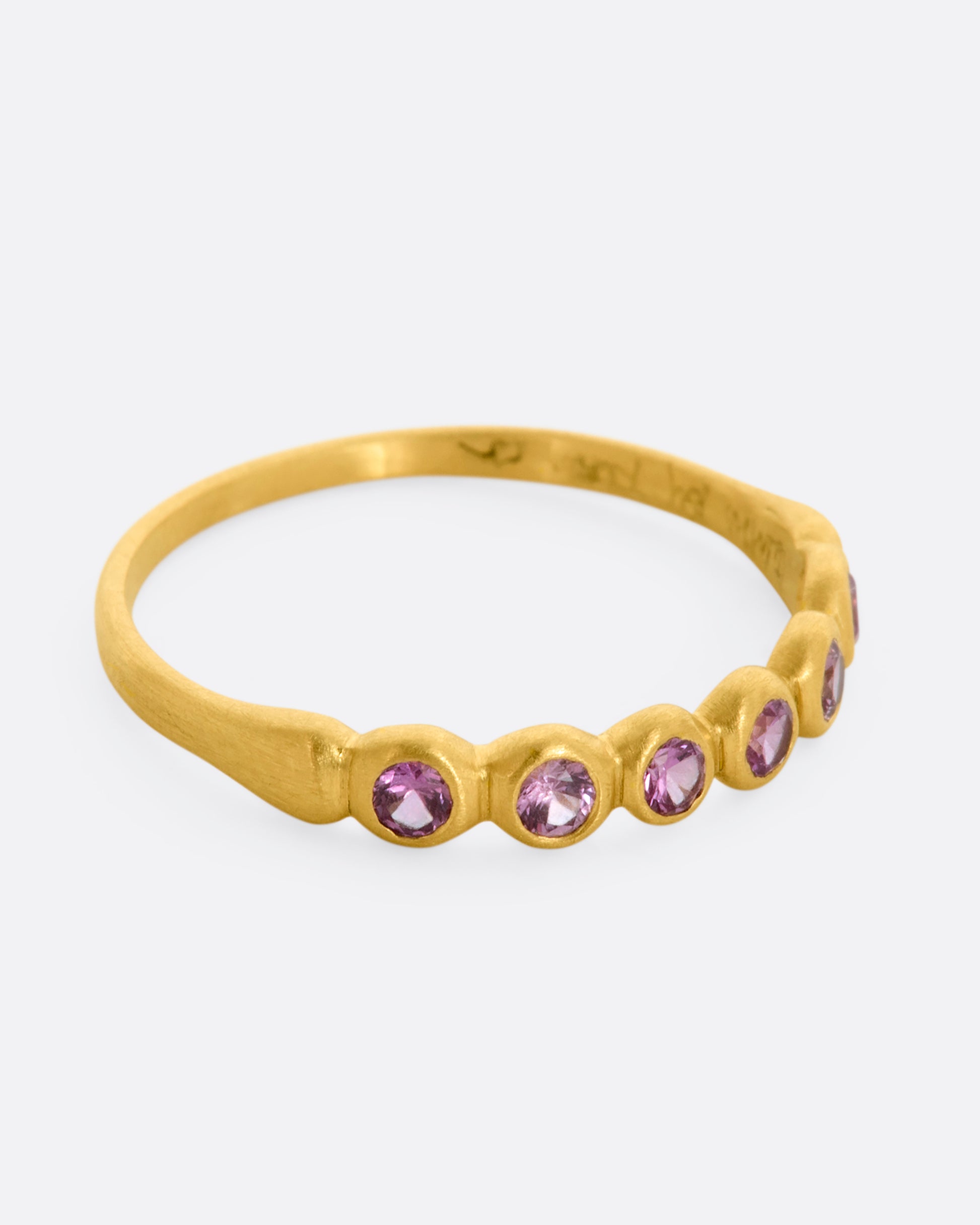 A yellow gold band with a row of pink sapphires. Shown from the side.