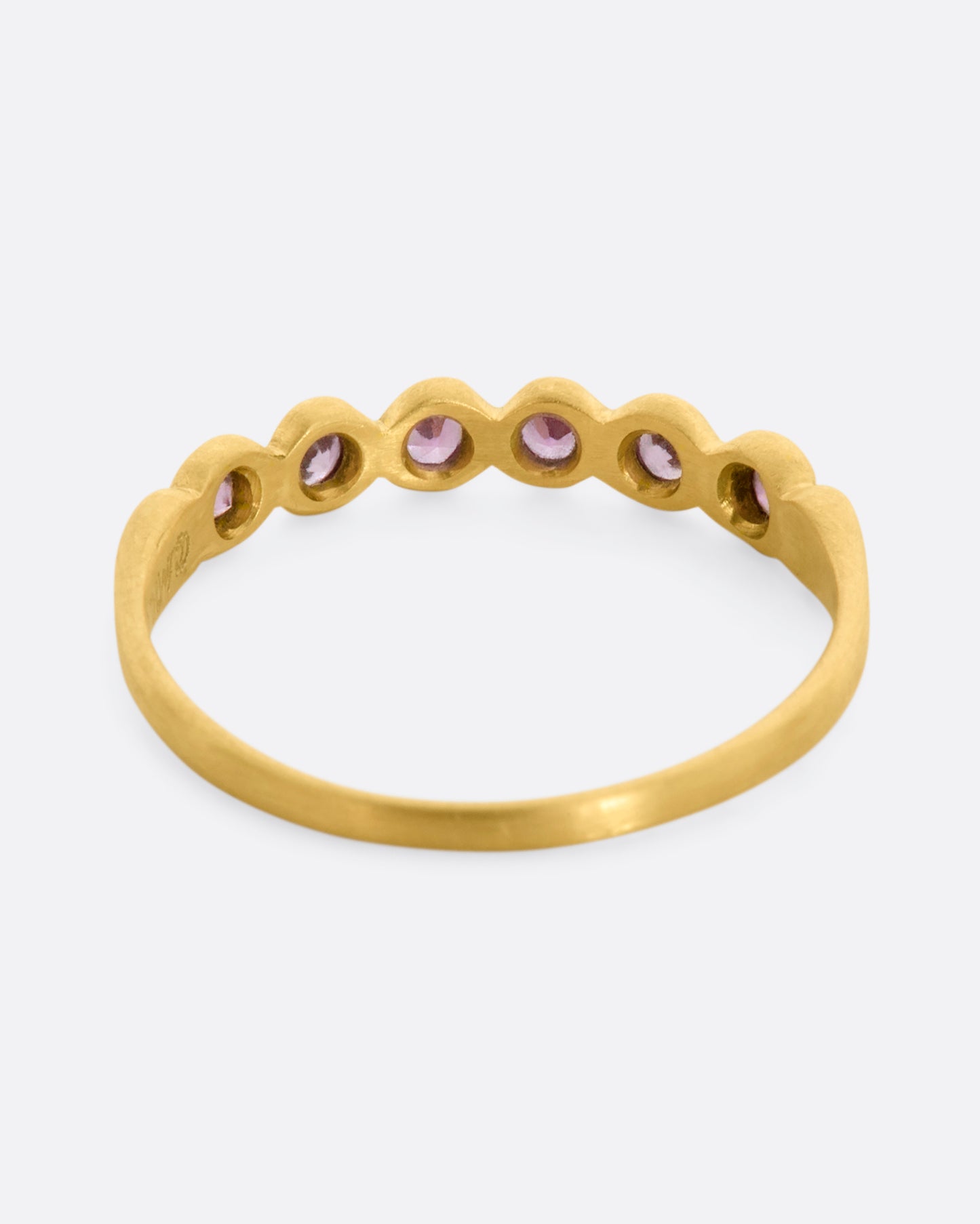 A yellow gold band with a row of pink sapphires. Shown from the back.