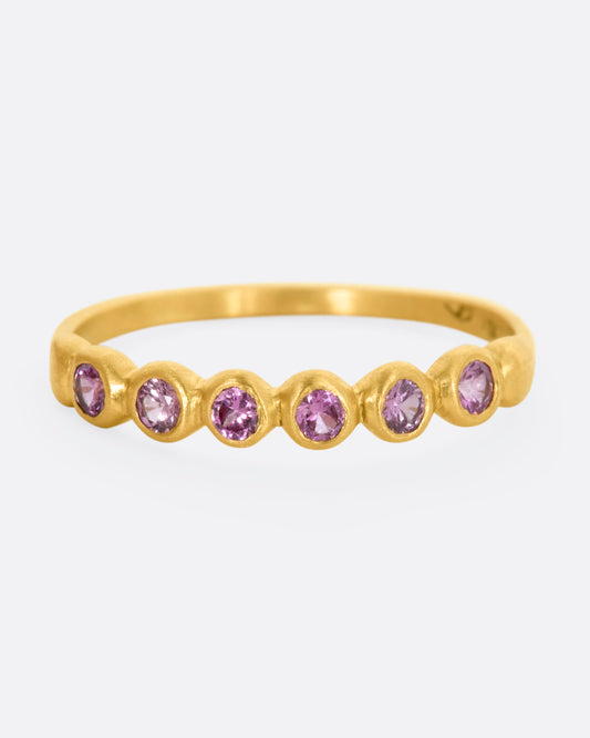 A yellow gold band with a row of pink sapphires. Shown from the front.