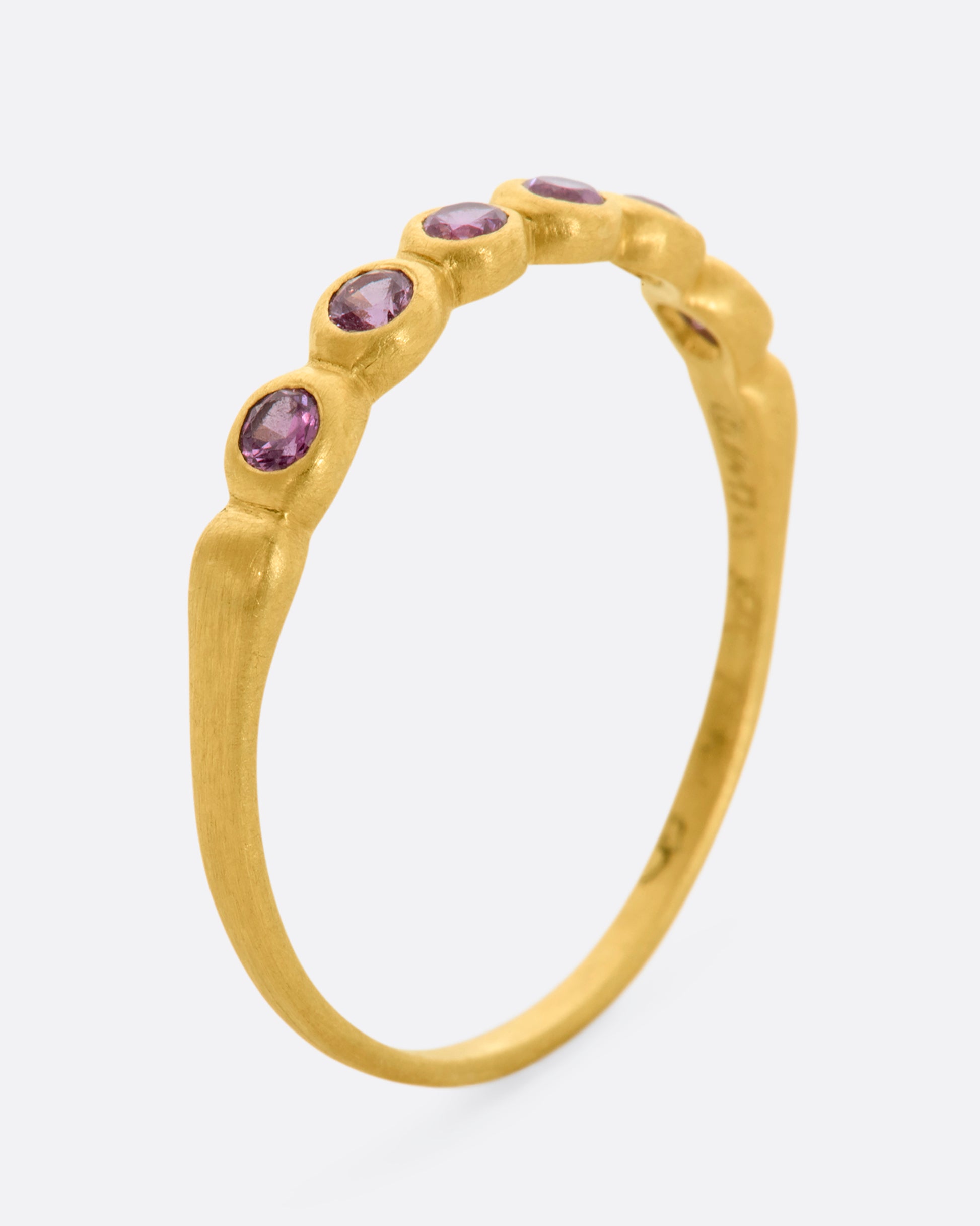 A yellow gold band with a row of pink sapphires. Shown from the side, standing up.