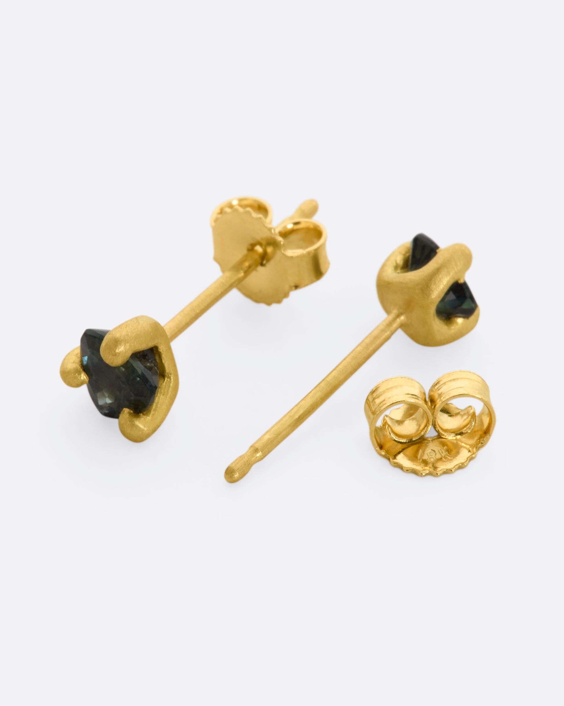 A pair of matte yellow gold prong set 4mm sapphire stud earrings. View laying flat showing the post and backing.