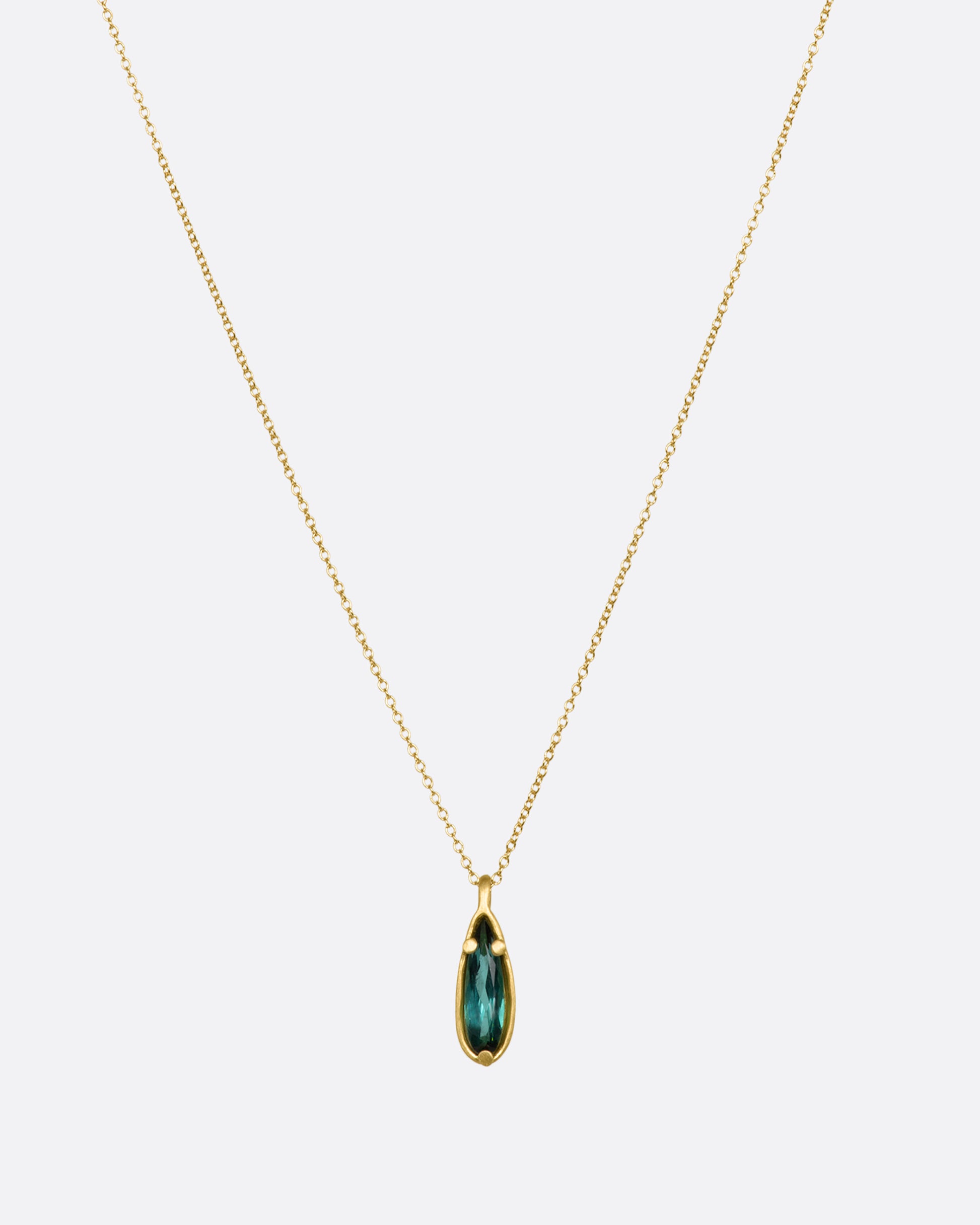 A matte yellow gold necklace with a large pear shaped teal tourmaline pendant. View from the front.