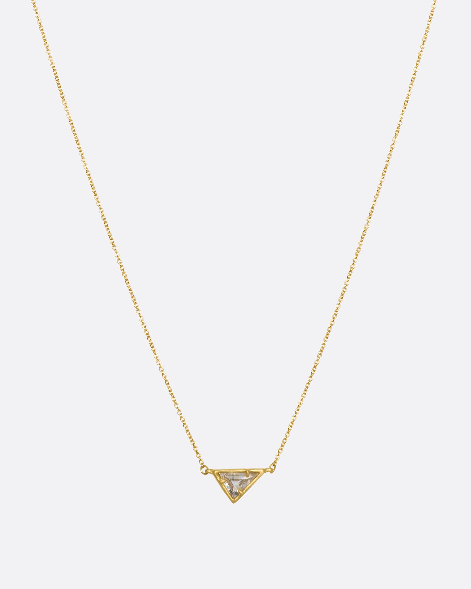 A yellow gold necklace with a triangular goshenite pendant. View from the front hanging with more chain showing.