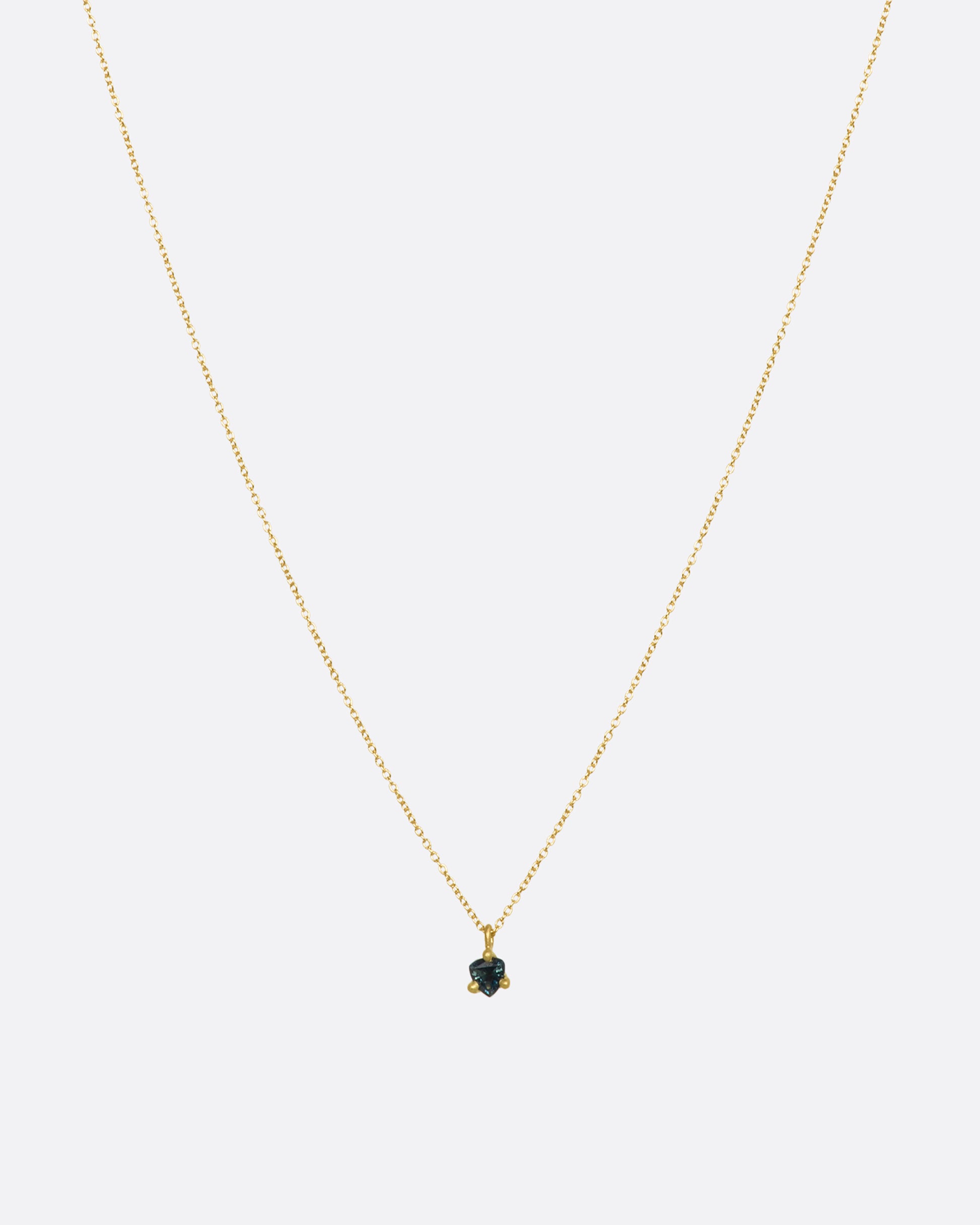 A matte yellow gold prong set triangle teal sapphire necklace. View from the front.