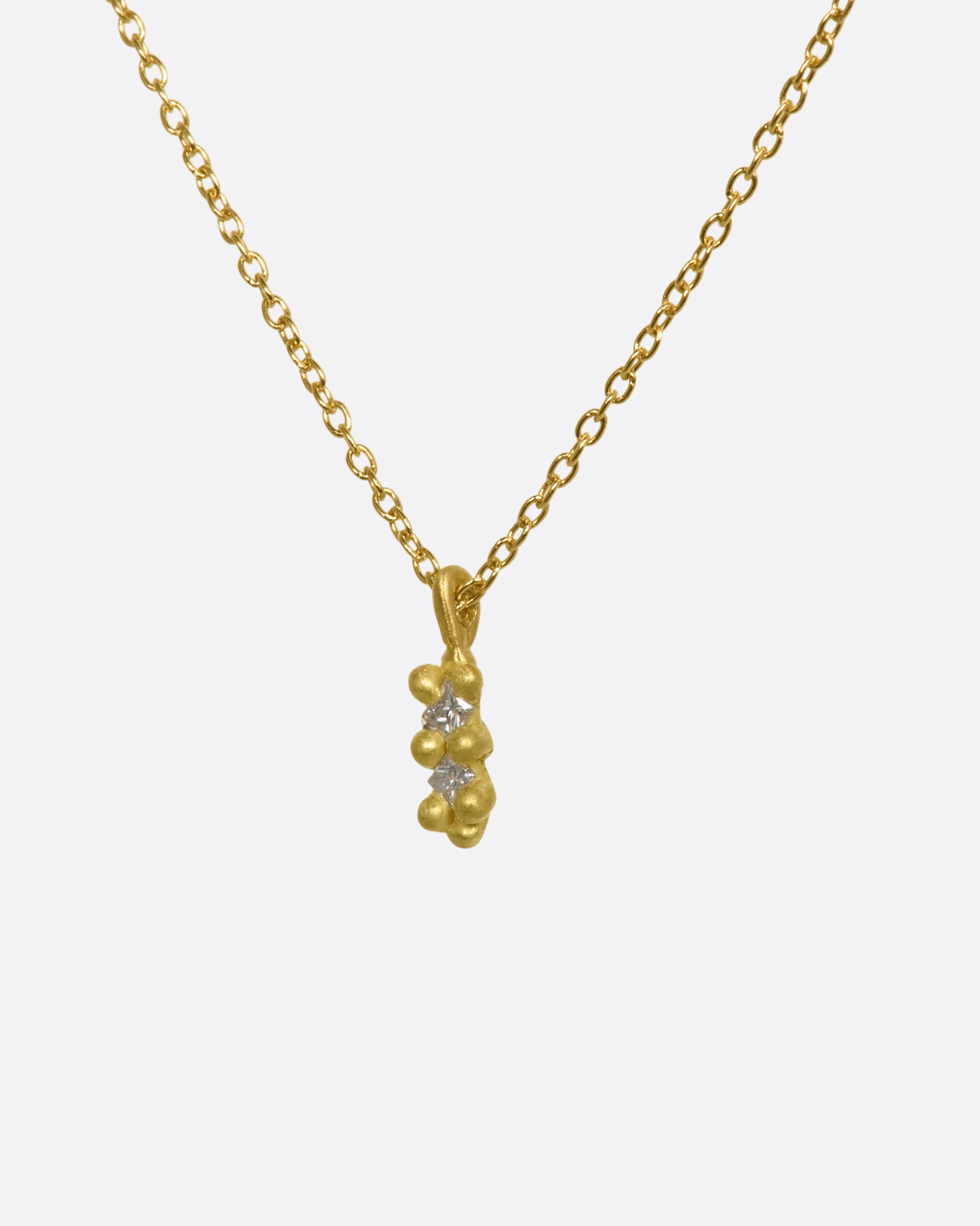 A yellow gold necklace with a double white diamond pendant. Shown from the side.