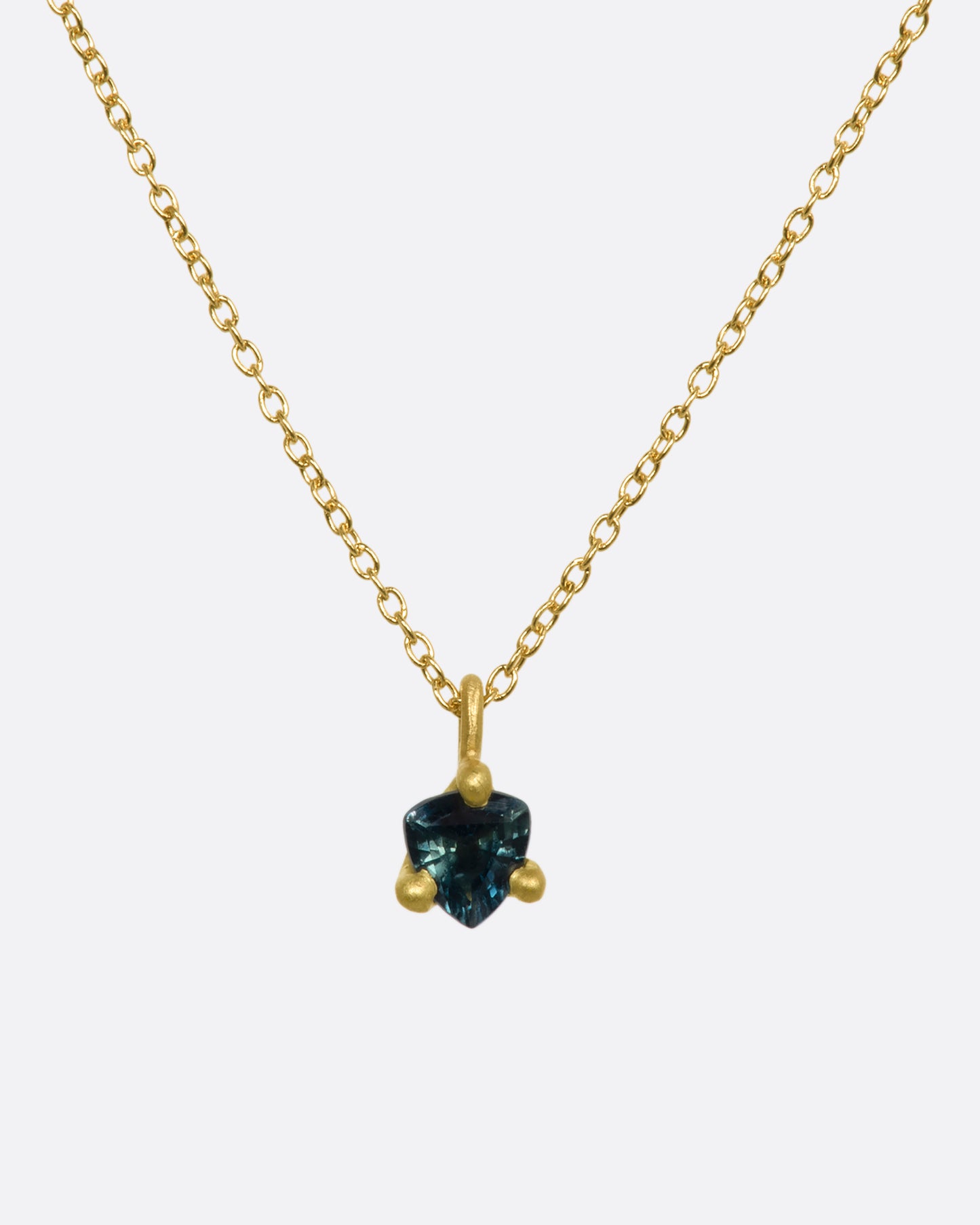 A matte yellow gold prong set triangle teal sapphire necklace. View from the front.