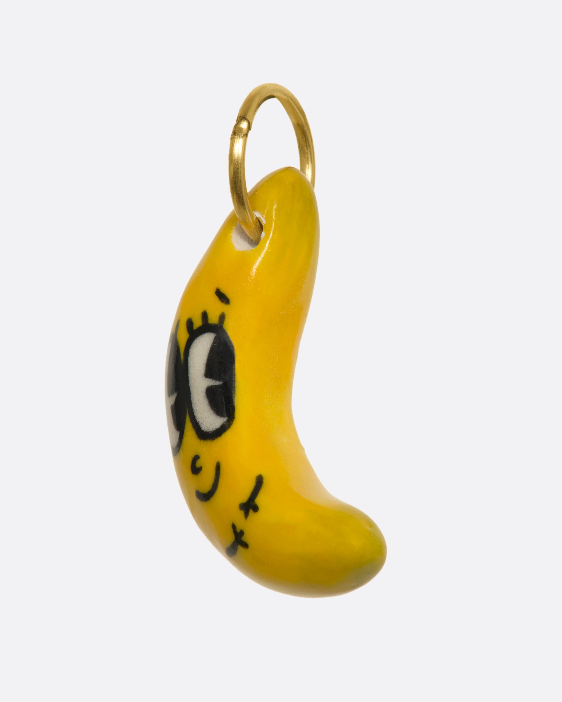 A yellow banana charm with a face and yellow gold bale. View from the side.