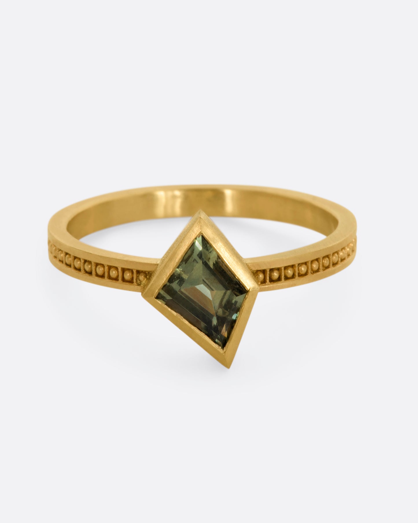 A yellow gold ring with a trapezoid green sapphire and raised dots in square shaped holes around the band. View from the front.