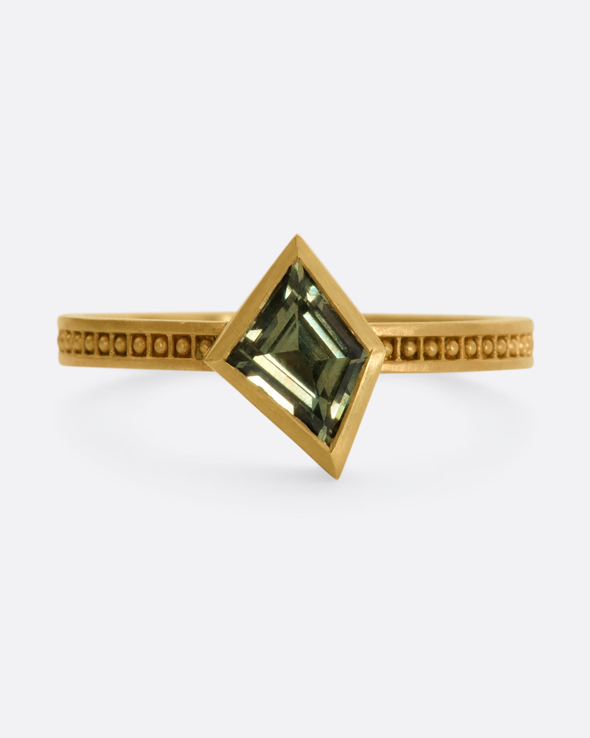 A yellow gold ring with a trapezoid green sapphire and raised dots in square shaped holes around the band. View from the front.