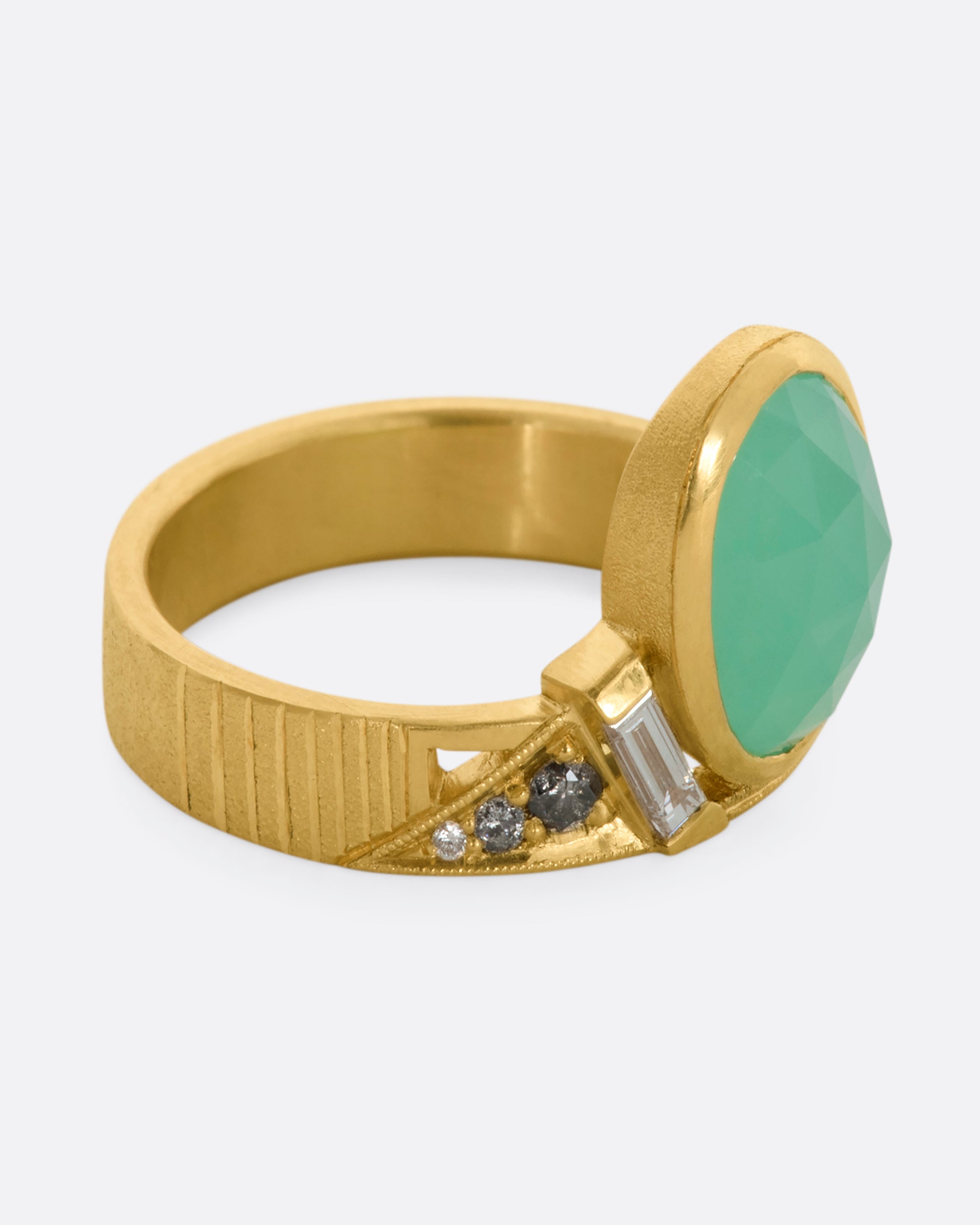 A yellow gold wide band ring with an oval chrysoprase, stacked baguette and round diamonds. View from the side.