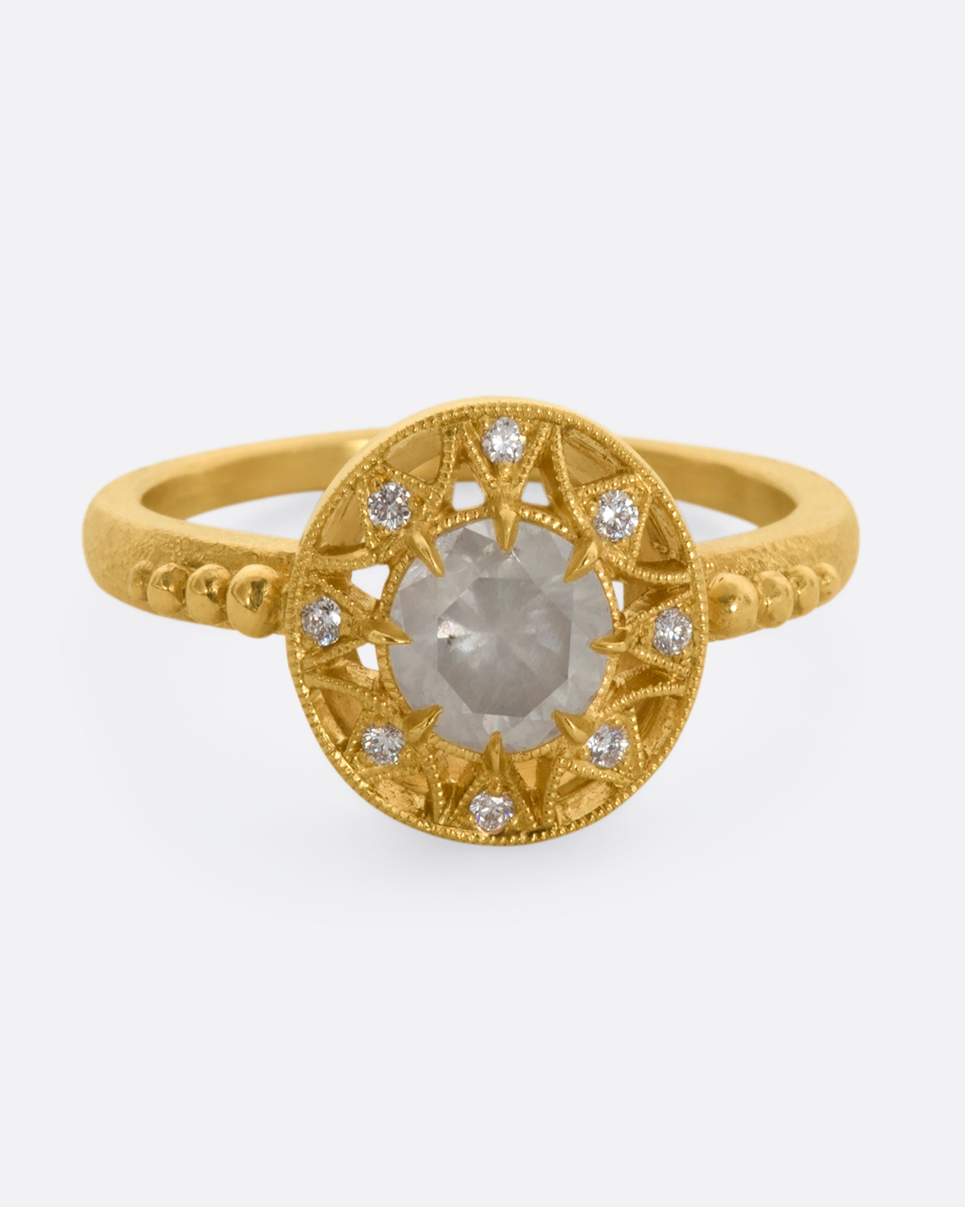 A yellow gold ring with a rose cut opalescent diamond at the center and a ring of brilliant cut diamonds around the face. View from the front.