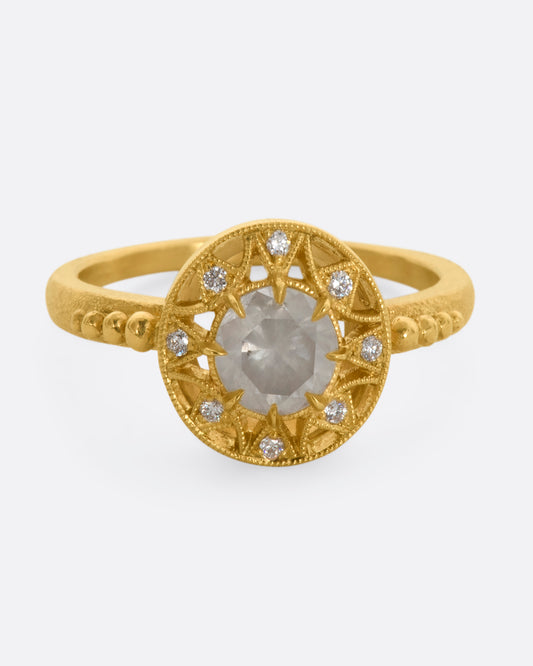 A yellow gold ring with a rose cut opalescent diamond at the center and a ring of brilliant cut diamonds around the face. View from the front.