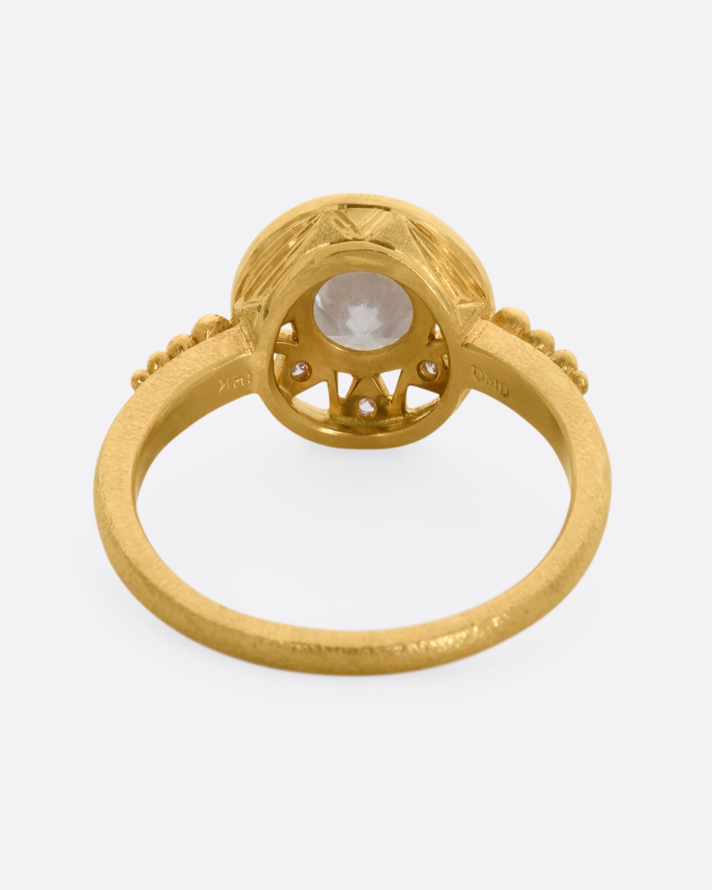 A yellow gold ring with a rose cut opalescent diamond at the center and a ring of brilliant cut diamonds around the face. View from the back.