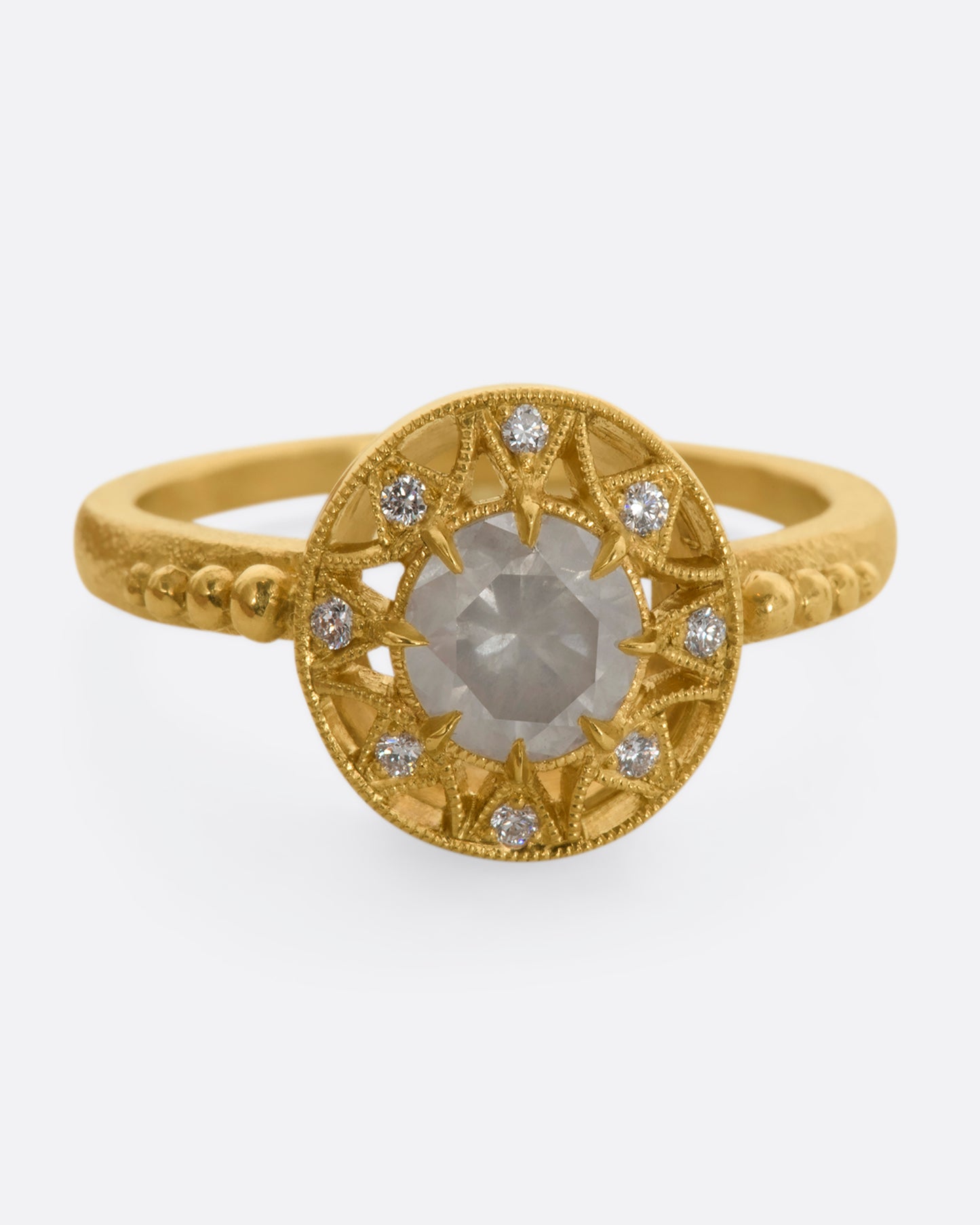 A yellow gold ring with a rose cut opalescent diamond at the center and a ring of brilliant cut diamonds around the face. View from the front close up.