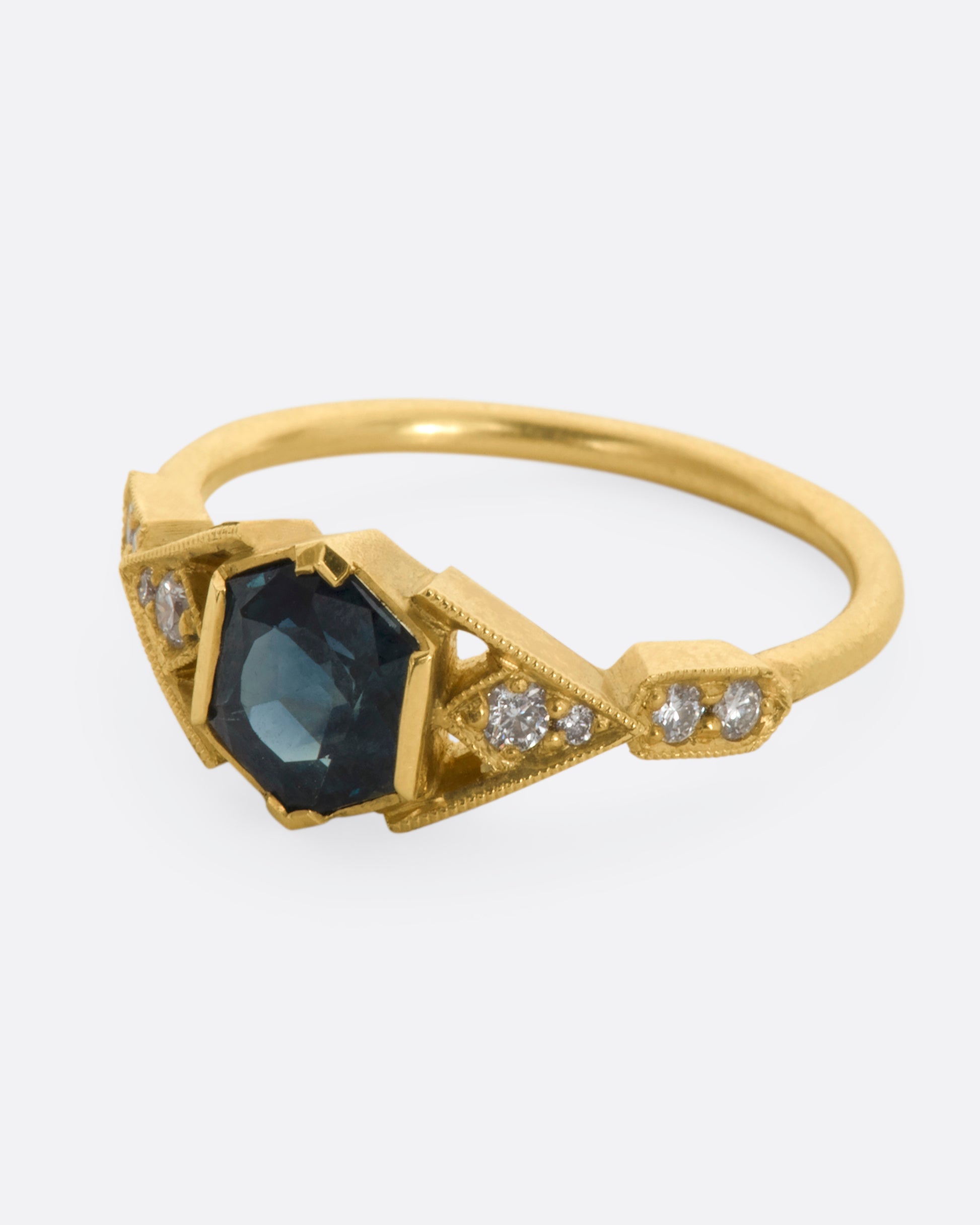 A yellow gold ring with deep teal sapphire and diamonds. View from the side.