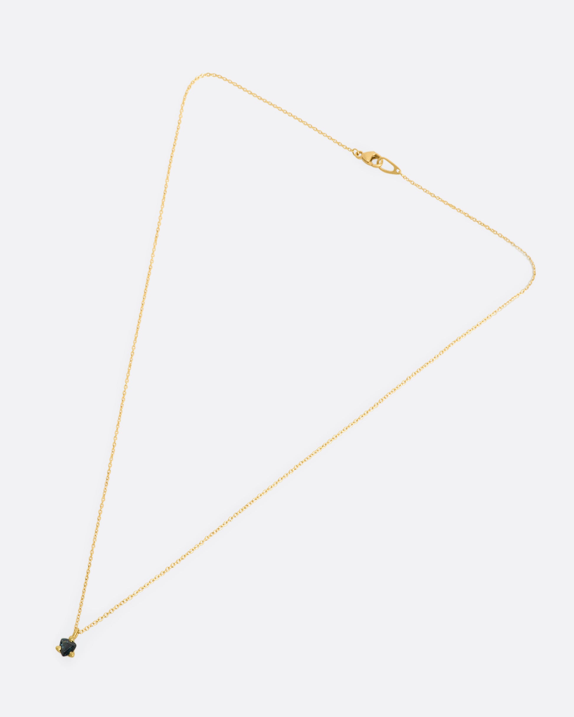 A matte yellow gold prong set triangle teal sapphire necklace. View of full necklace, laying flat.