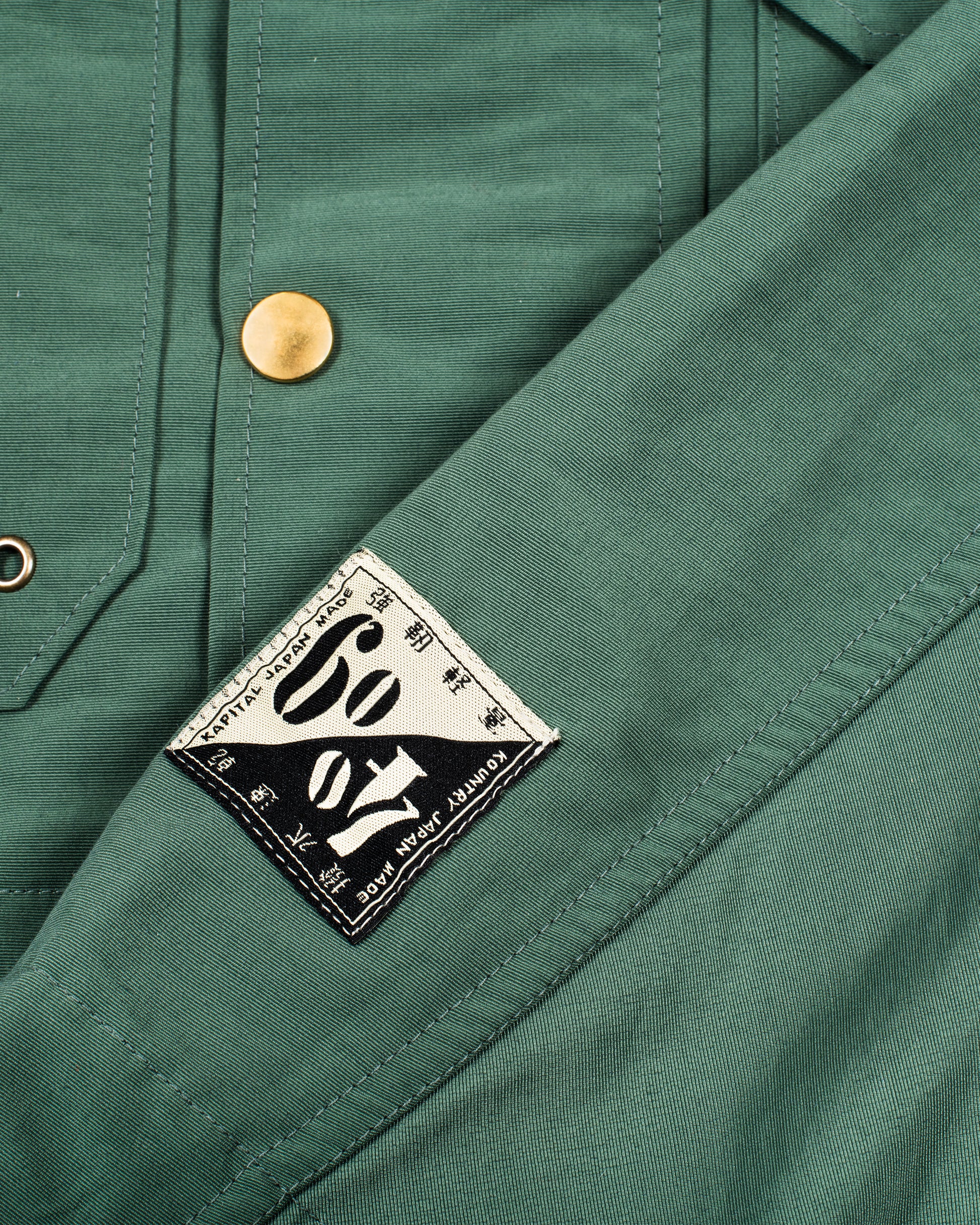 Cropped and hooded rain coat with two front pockets. View of the logo patch.