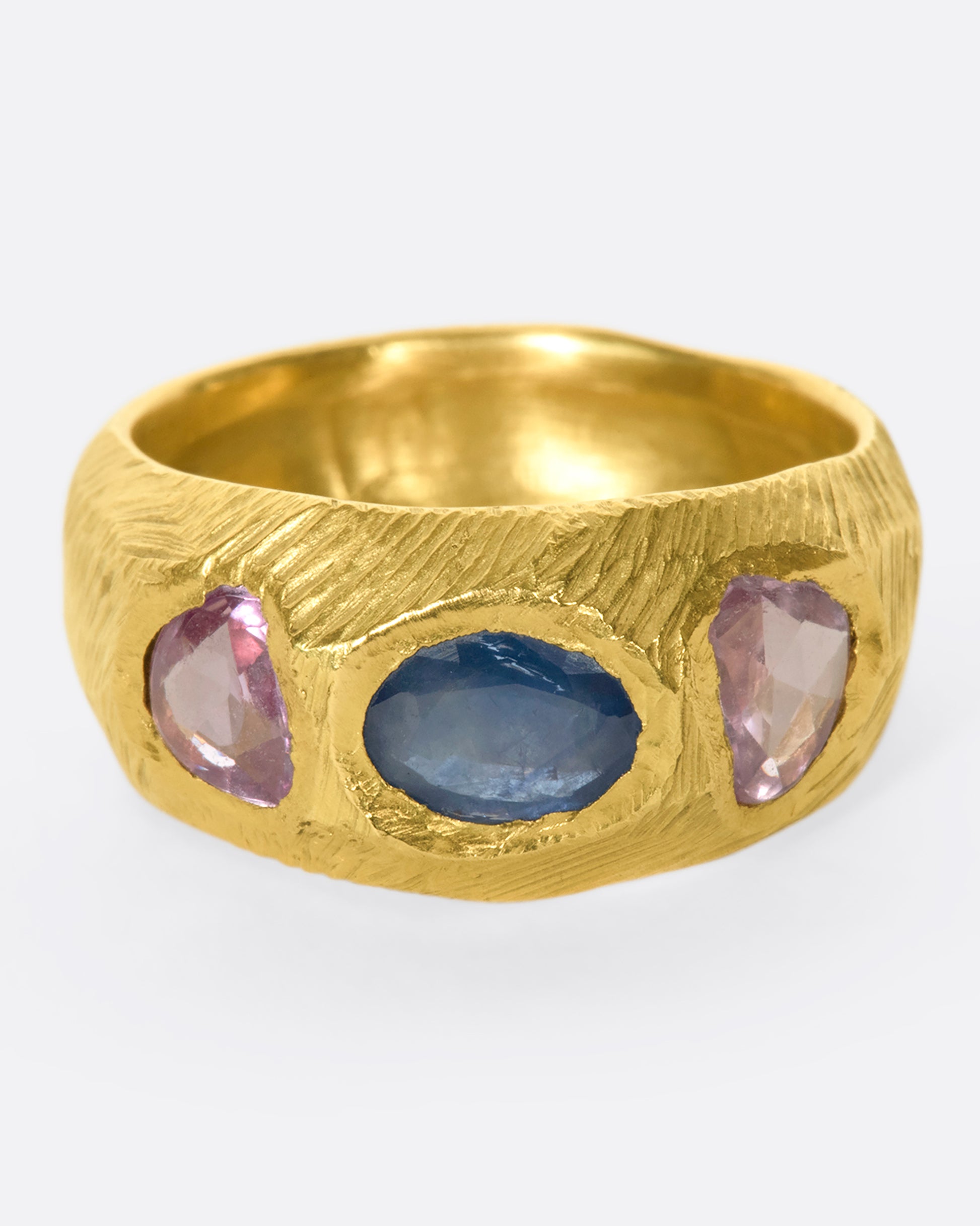 This hand carved 18k gold band is inlaid with an oval blue sapphire, flanked by beautiful pink sapphires