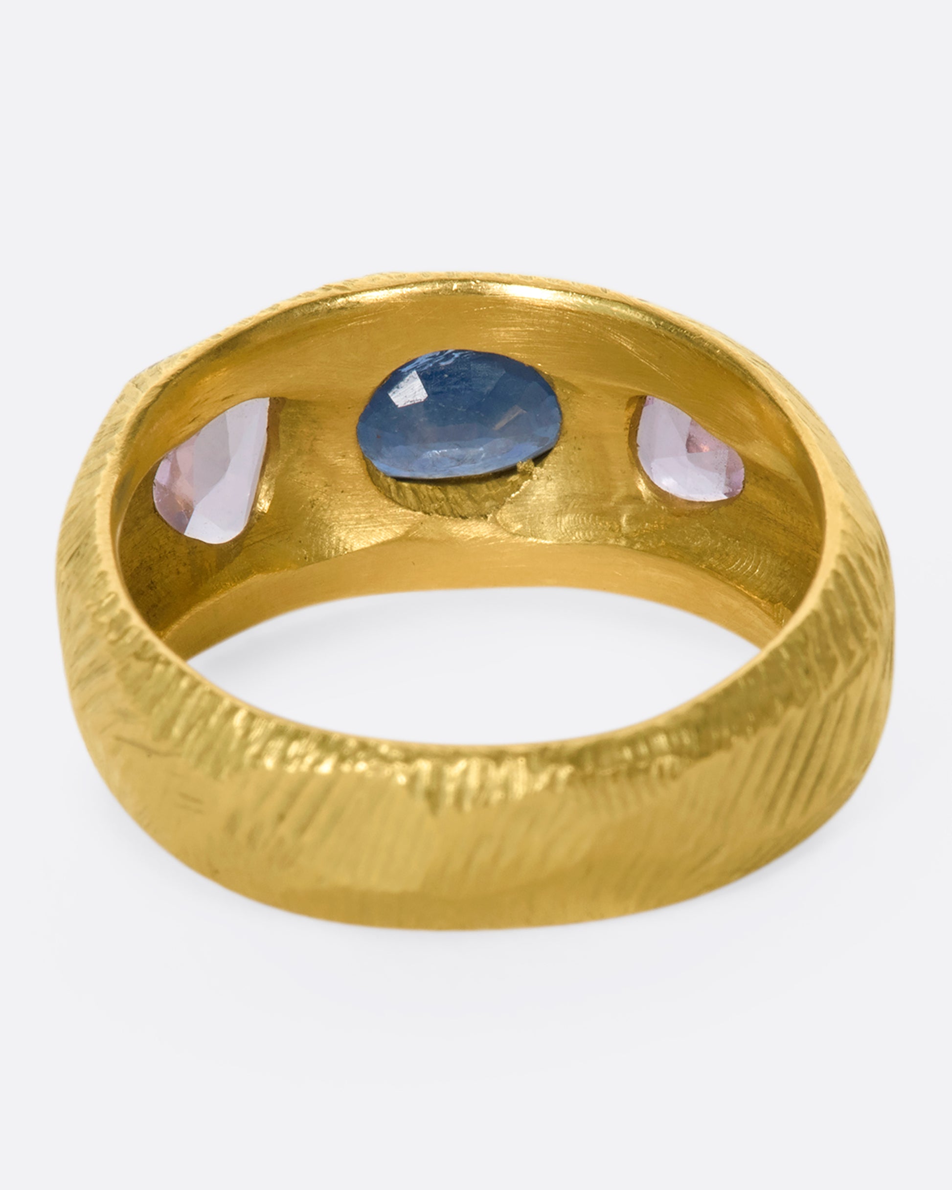 This hand carved 18k gold band is inlaid with an oval blue sapphire, flanked by beautiful pink sapphires