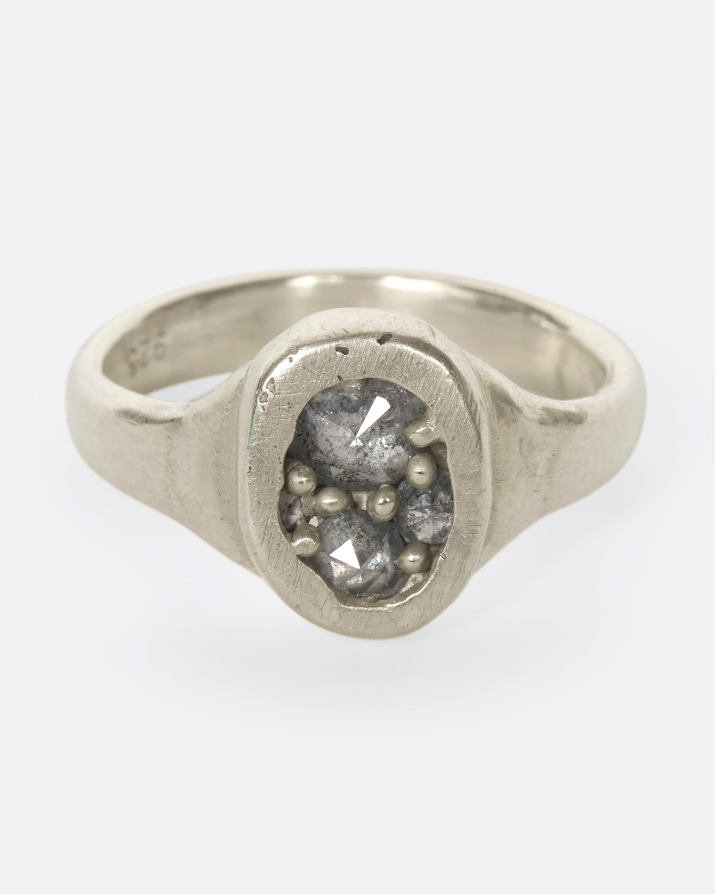 A slightly overhead view of an oval silver ring with grey diamonds.