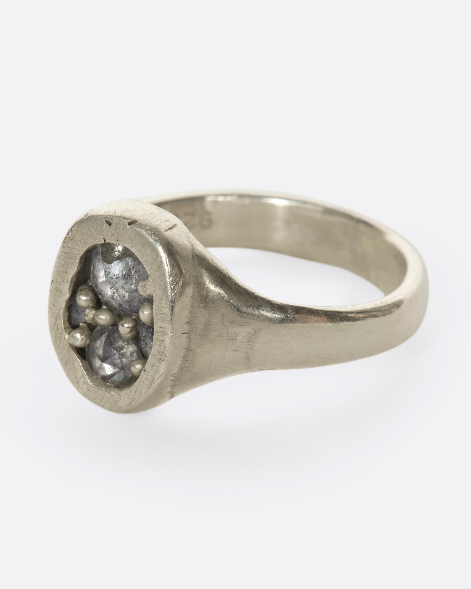 A left side view of an oval silver ring with grey diamonds.