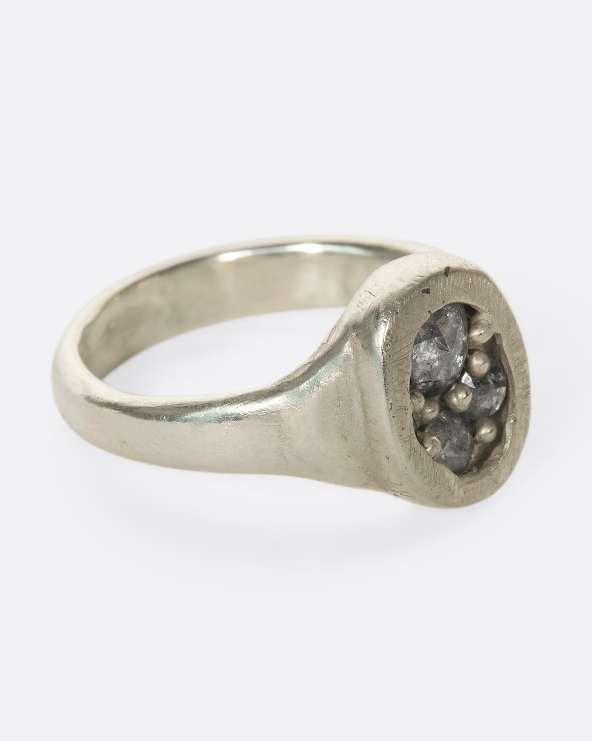 A right side view of an oval silver ring with grey diamonds.