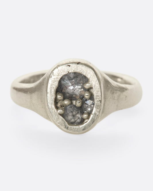 A close up of an oval silver ring with grey diamonds.