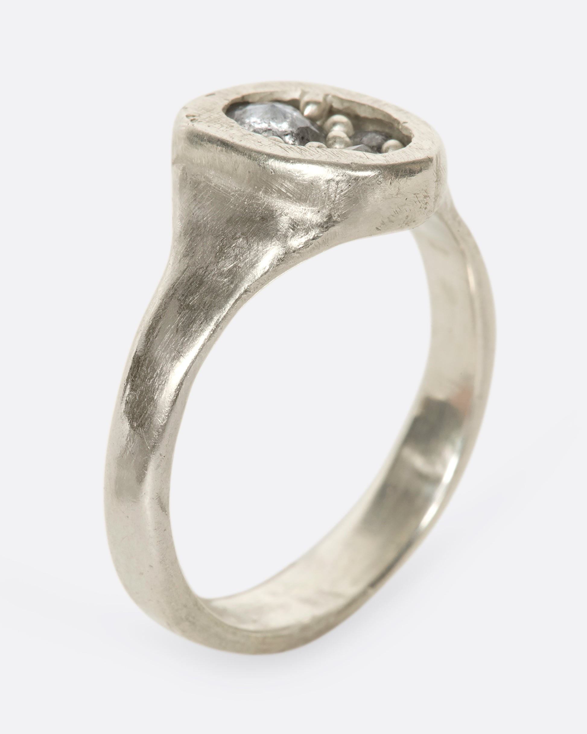 An oval silver ring with grey diamonds sitting upright on its band.