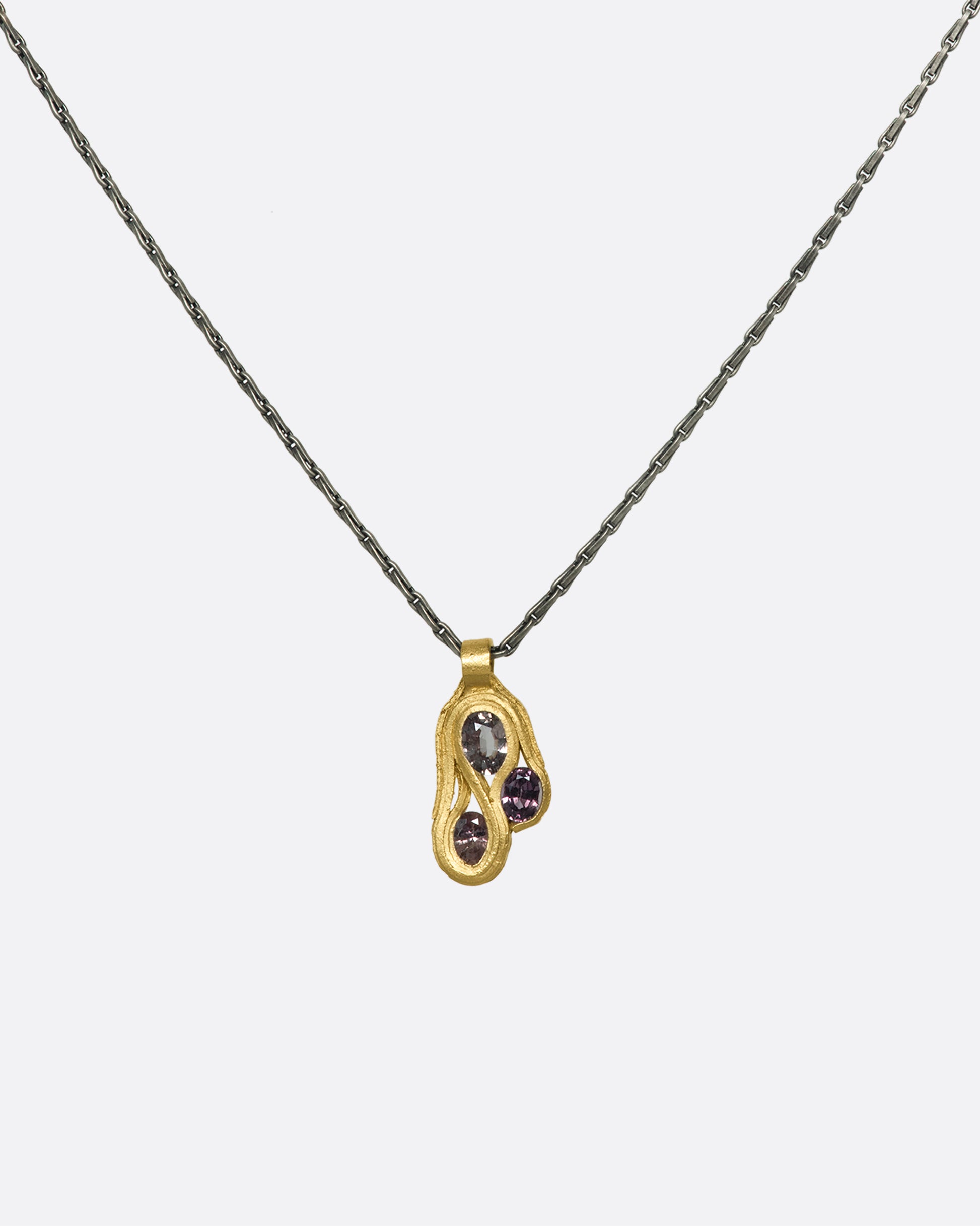 A hanging gold pendant with three pink sapphires on a darkened silver chain.