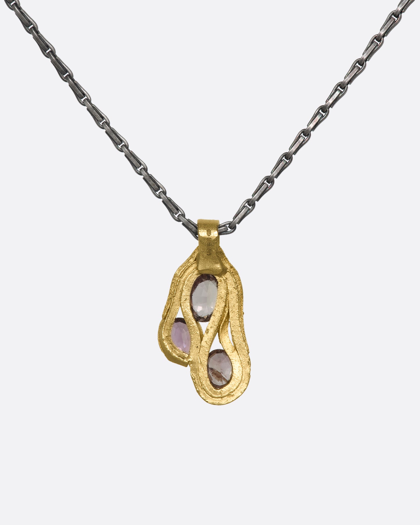 The bank of a hanging gold pendant with three pink sapphires on a darkened silver chain.