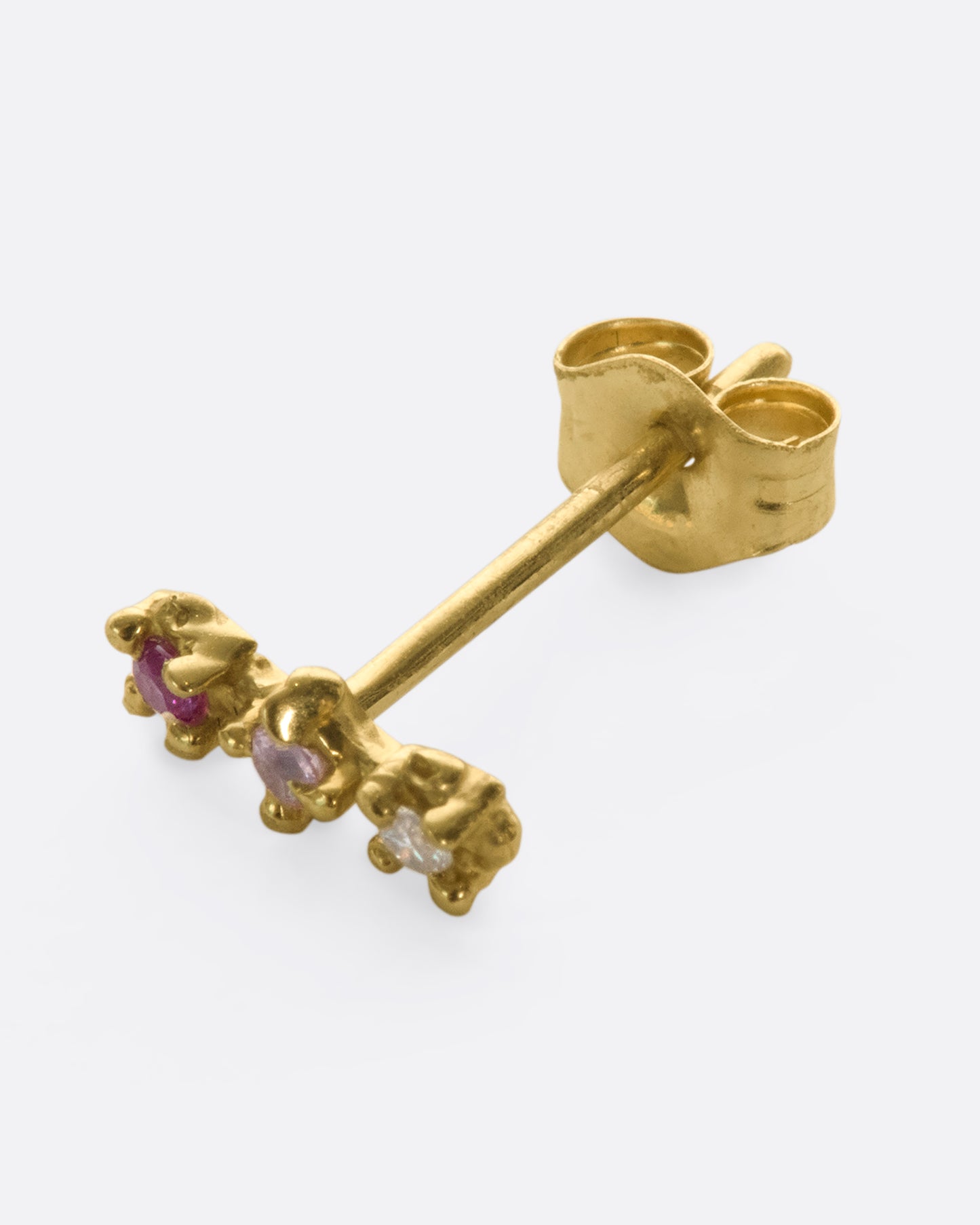 A 14k gold bar stud embellished with a ruby, pink sapphire, and diamond