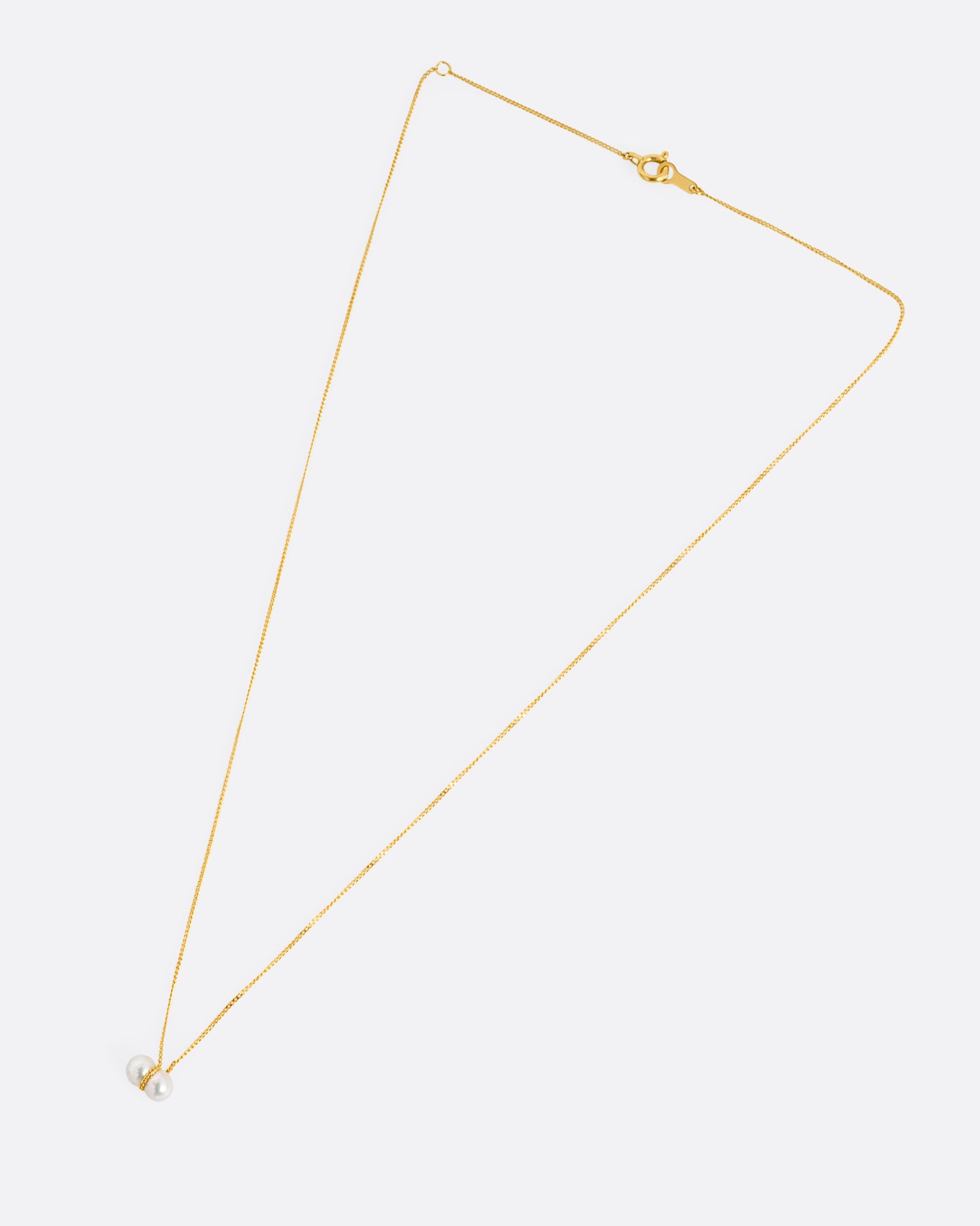 A yellow gold necklace with a small double pearl pendant. Shown laying flat.