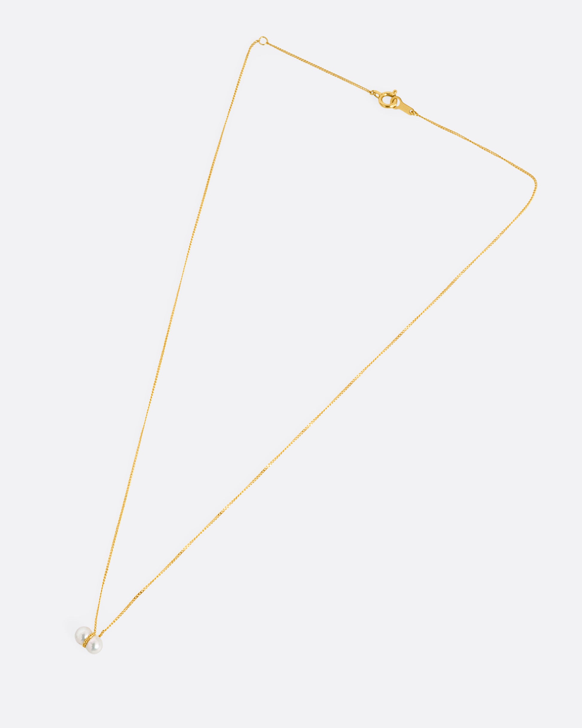 A yellow gold necklace with a small double pearl pendant. Shown laying flat.