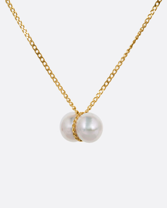 A yellow gold necklace with a small double pearl pendant. Shown from the front.