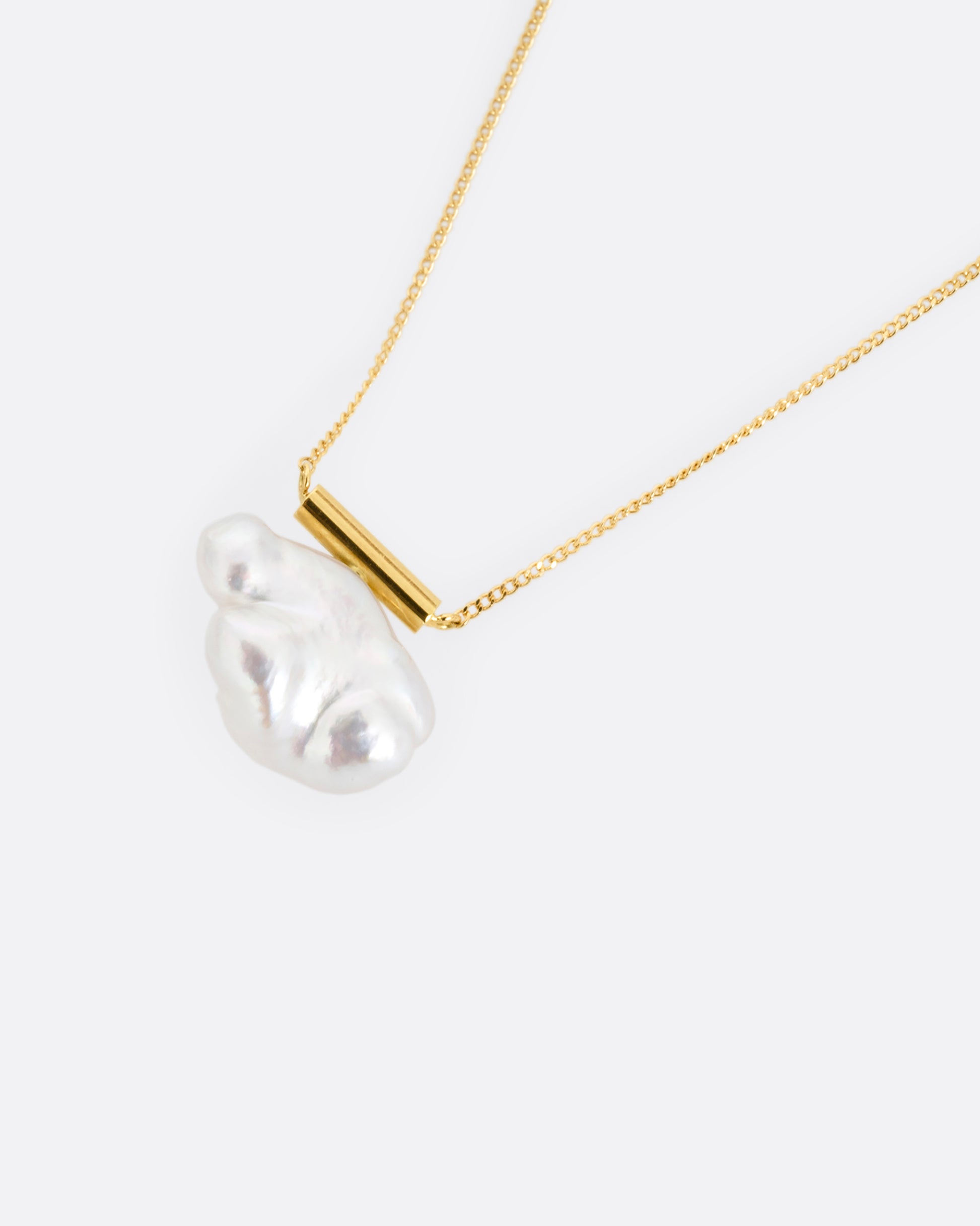 A yellow gold cable chain necklace with a gold bar and freeform pearl. Shown from the front.