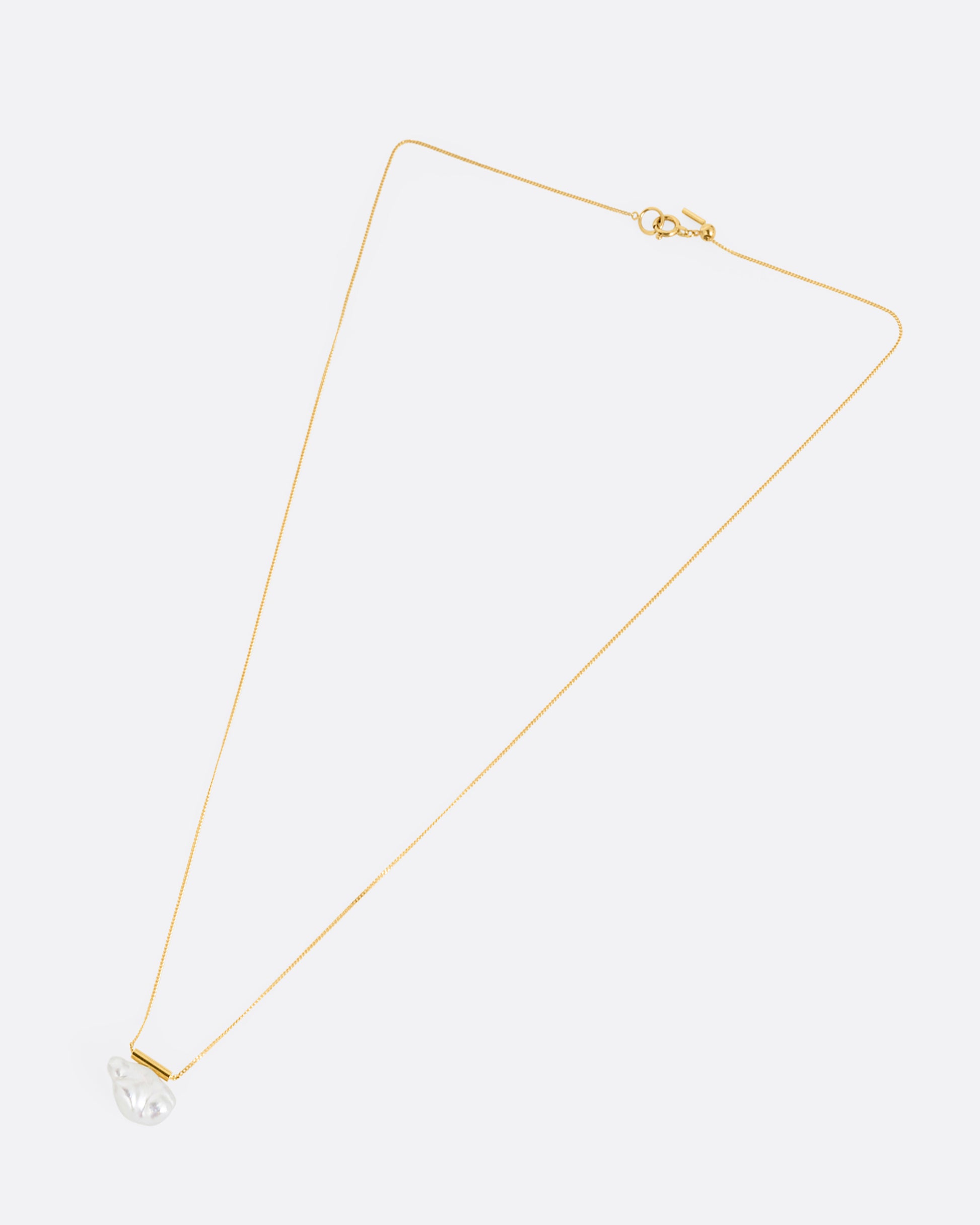 A yellow gold cable chain necklace with a gold bar and freeform pearl. Shown from the front.