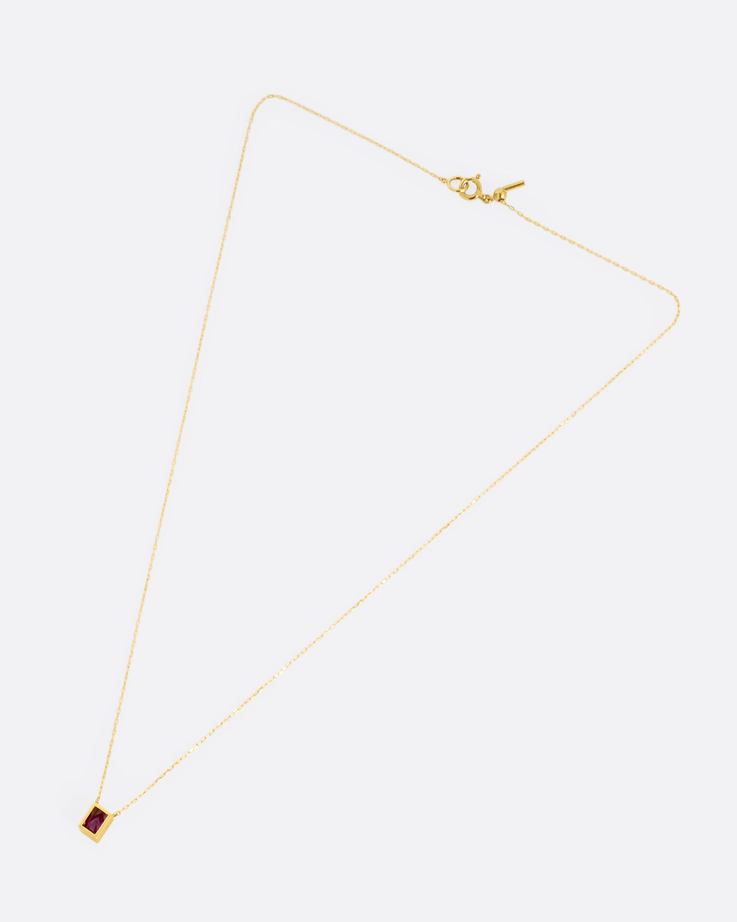 A yellow gold cable chain necklace with an open rectangular setting and a teardrop shaped ruby. Shown from the front.