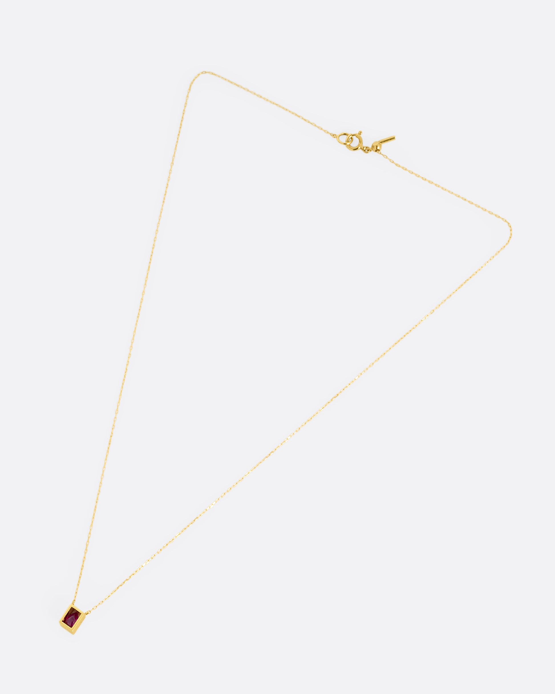 A yellow gold cable chain necklace with an open rectangular setting and a teardrop shaped ruby. Shown from the front.
