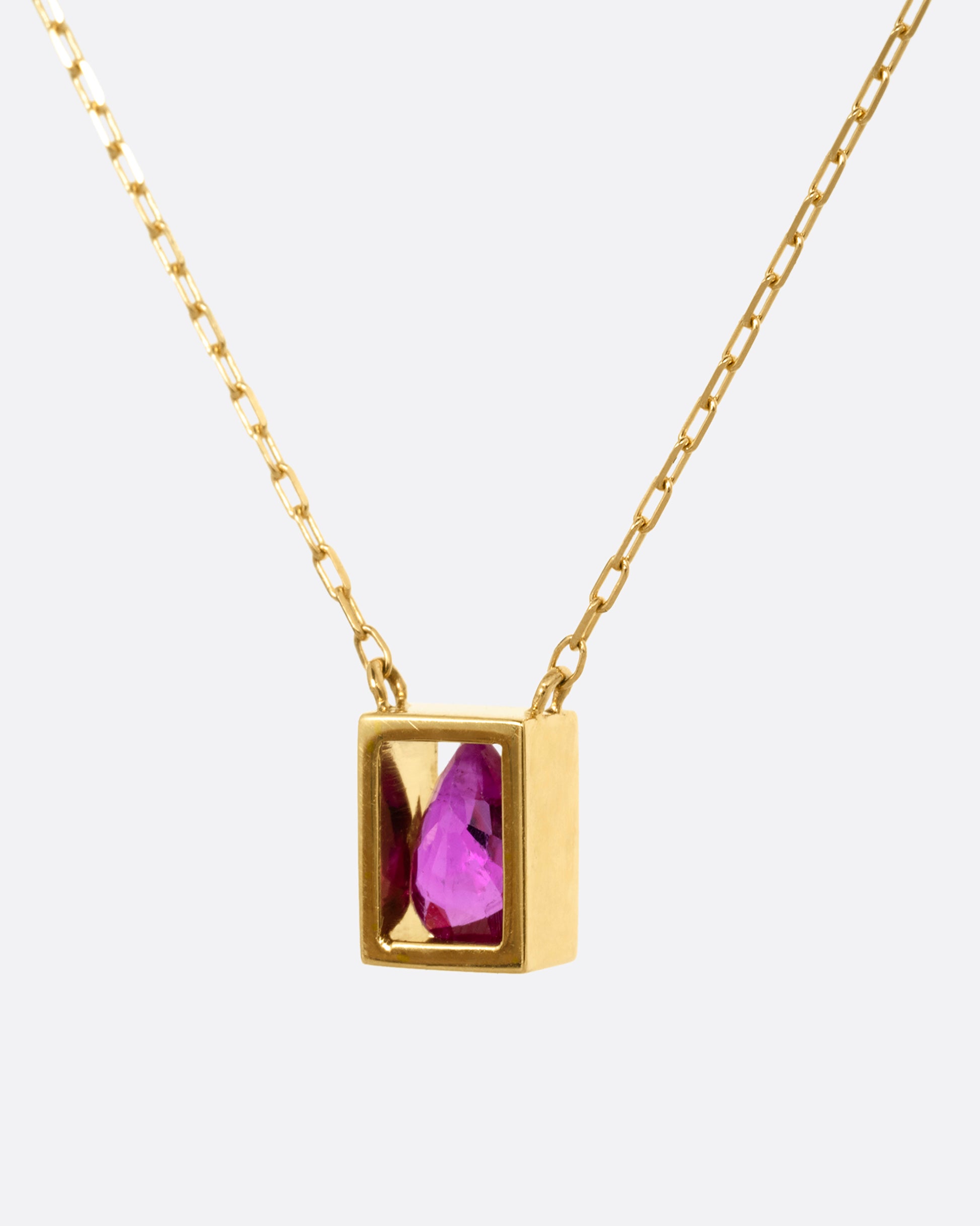 A yellow gold cable chain necklace with an open rectangular setting and a teardrop shaped ruby. Shown from the side.