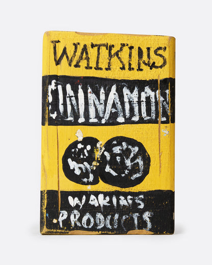 A yellow and black hand painted wooden box with the text 'WATKIN'S CINNAMON', shown from the back.