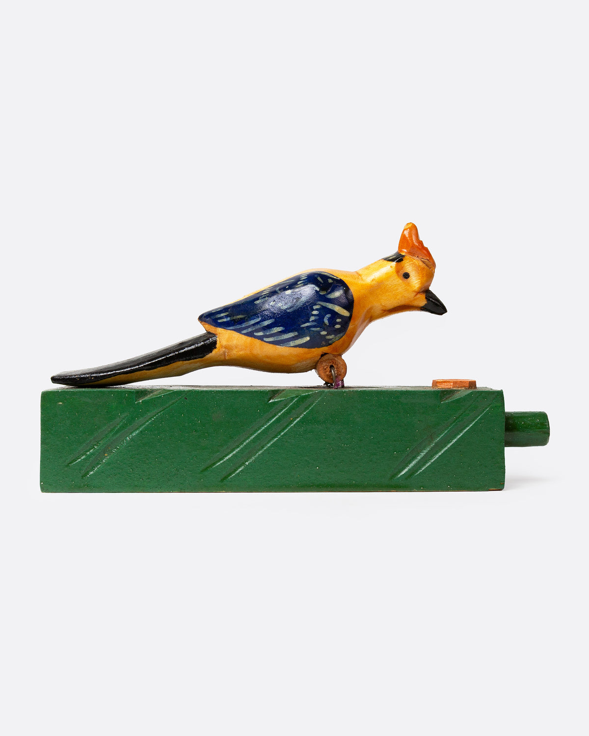 A wooden folk art toy with a yellow and blue woodpecker on a green base shown from the side.