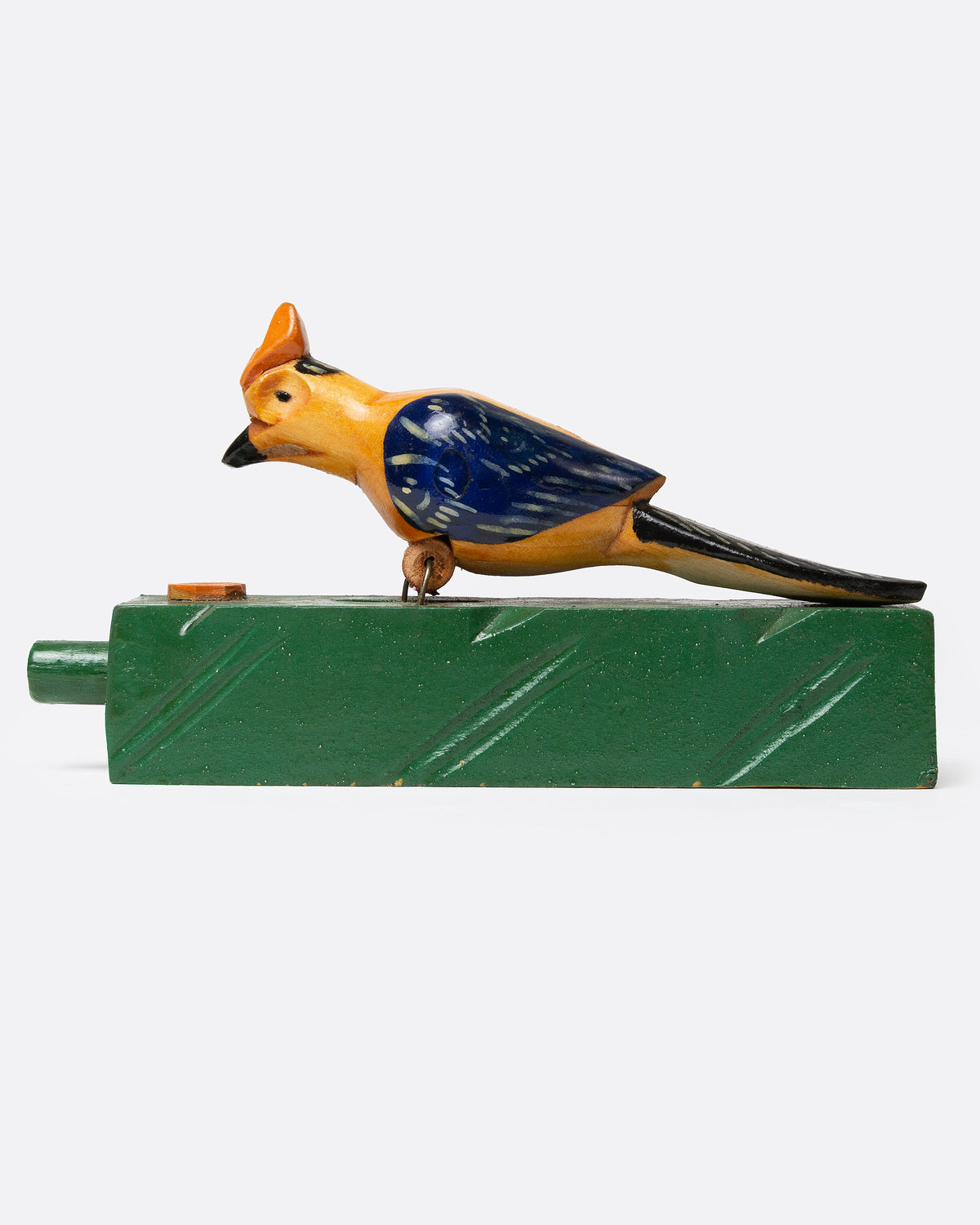 A wooden folk art toy with a yellow and blue woodpecker on a green base, shown from the side.