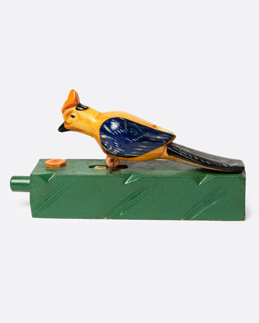 A wooden folk art toy with a yellow and blue woodpecker on a green base, shown from the side.