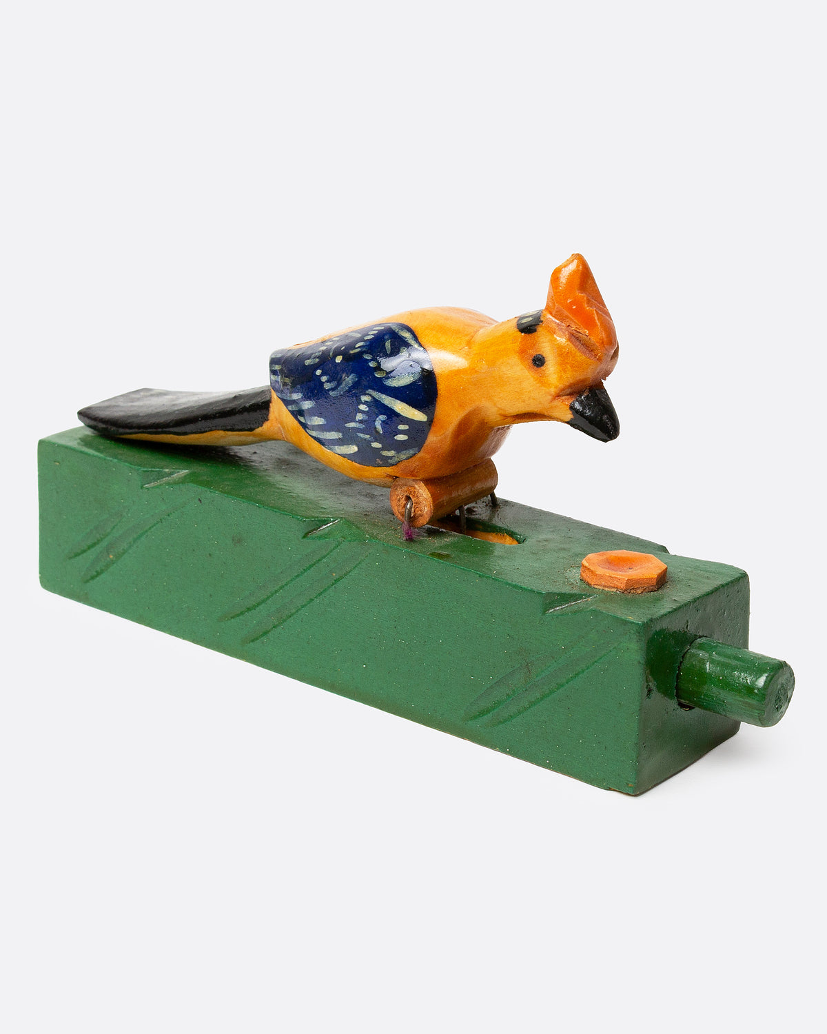 A wooden folk art toy with a yellow and blue woodpecker on a green base, shown from the side.
