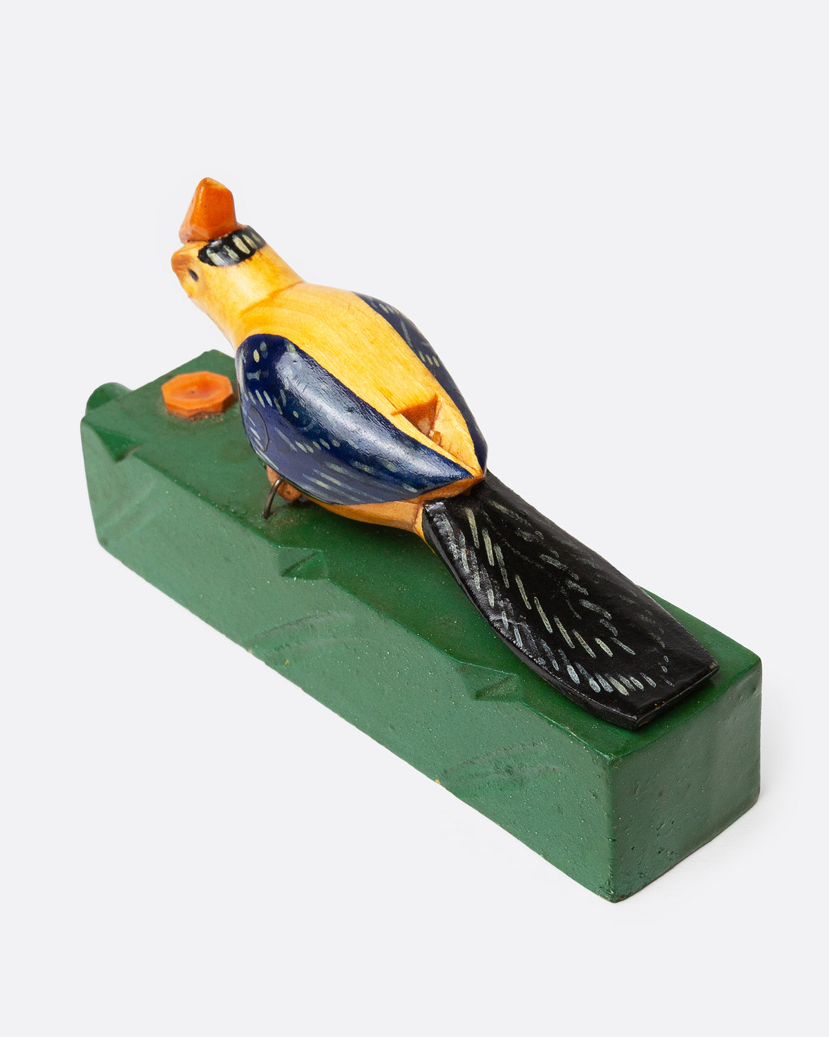 A wooden folk art toy with a yellow and blue woodpecker on a green base, shown from the back.