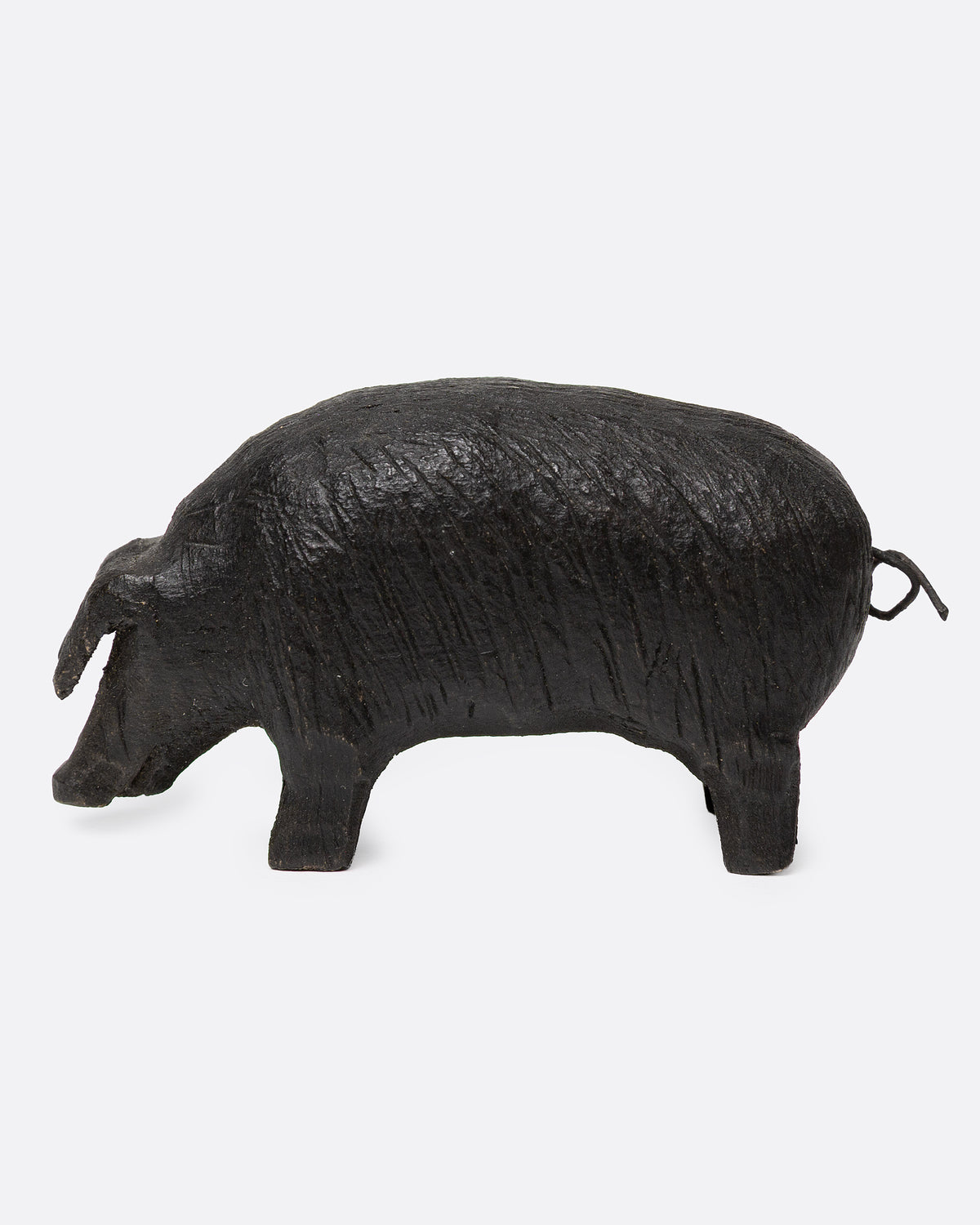 A wooden hand carved pig figurine with a wire tail, shown from the side.